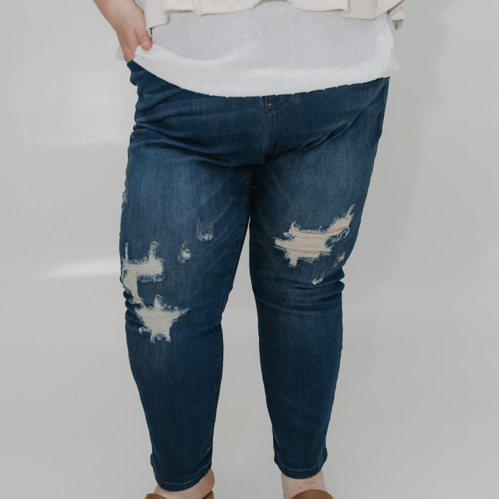 Person wearing blue distressed jeans and brown sandals on a plain background