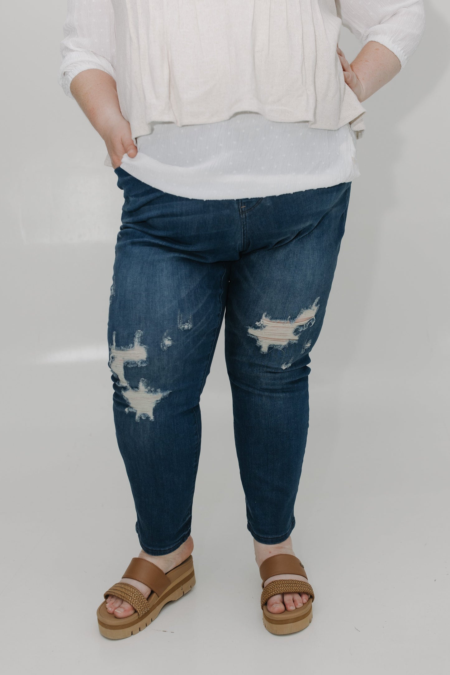 Person wearing blue distressed jeans and brown sandals on a plain background