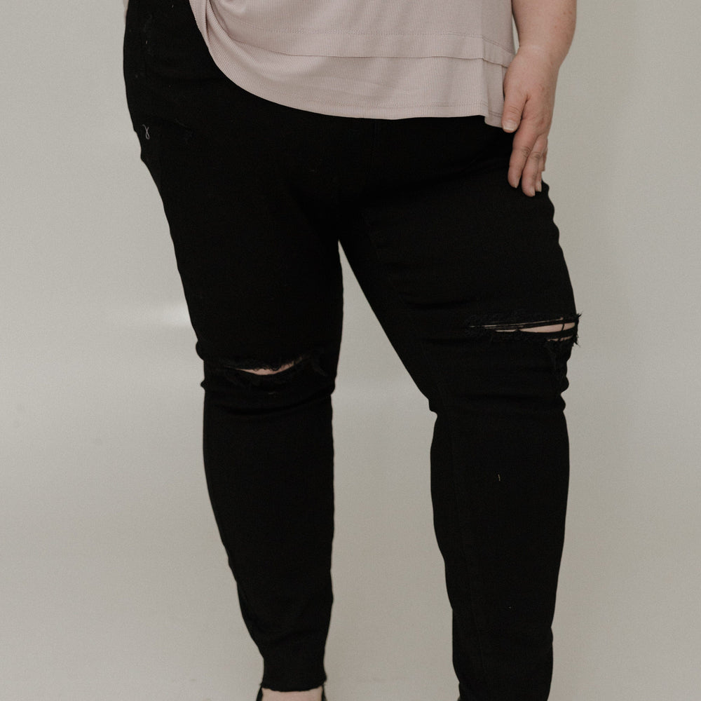 Person wearing black distressed jeans and a beige top on a plain background