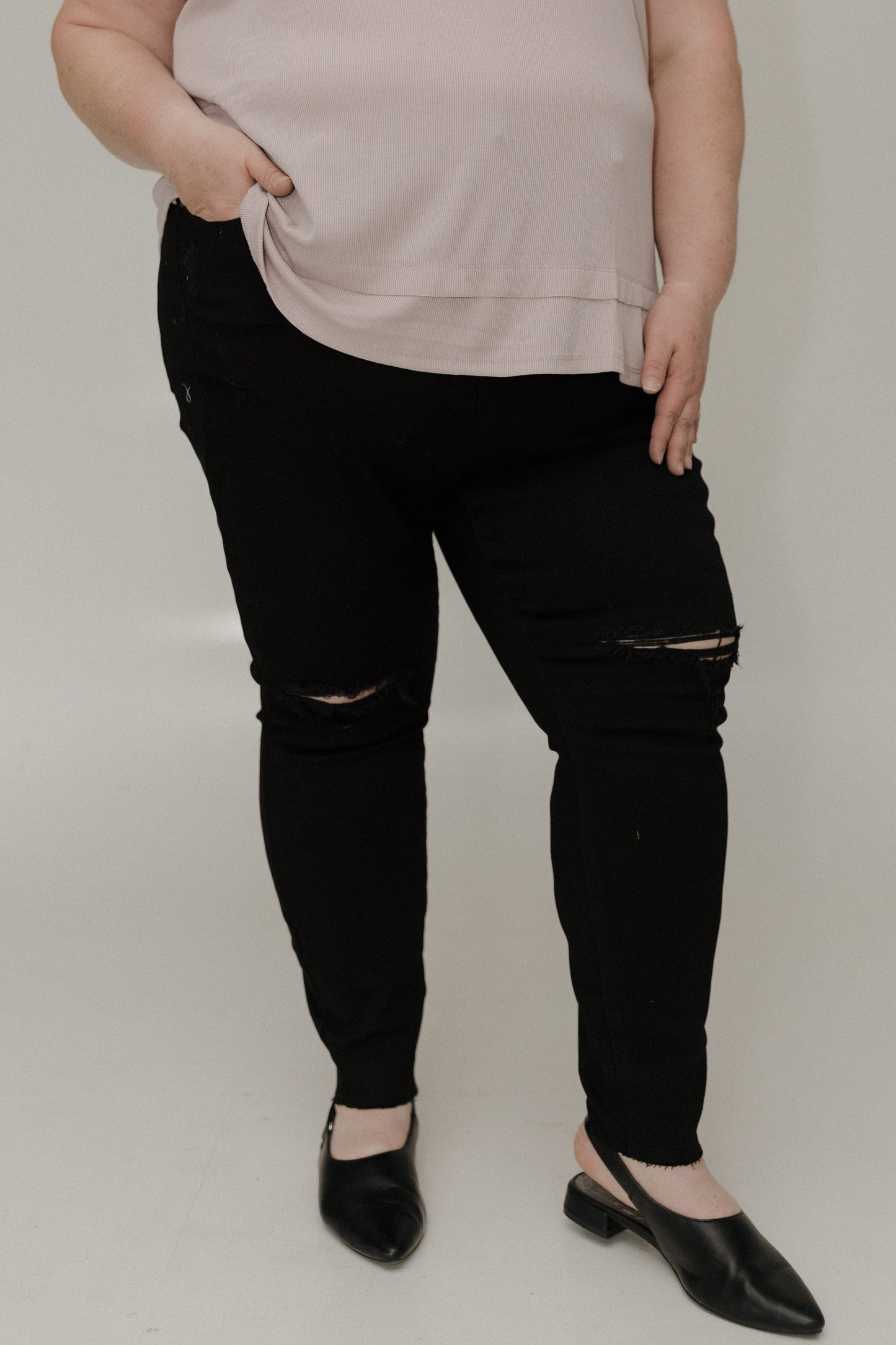 Person wearing black distressed jeans and a beige top on a plain background