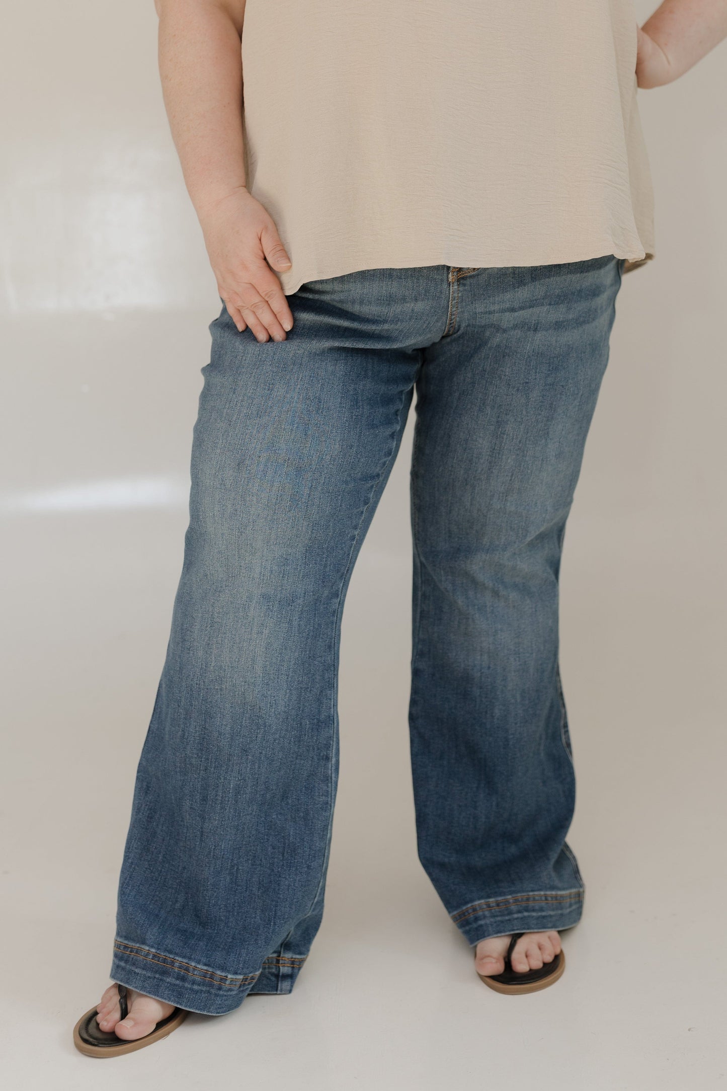 Person wearing blue jeans and a beige top on a plain background