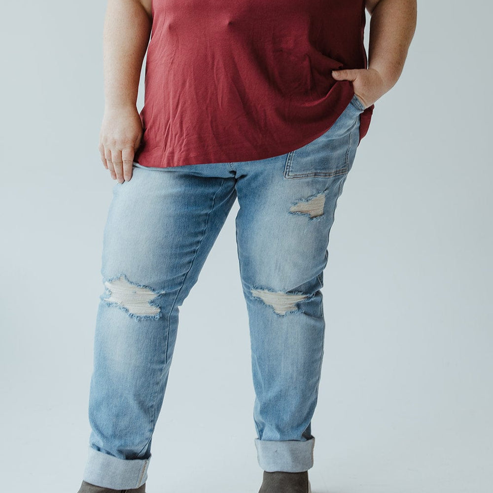 A person rocking the plus-size cool girl look, wearing a red sleeveless top, Judy Blue High Waisted Destroyed Boyfriend Jeans in Medium Wash made from Judy Blue’s stretchy denim, and gray high-top sneakers with one hand in their pocket.