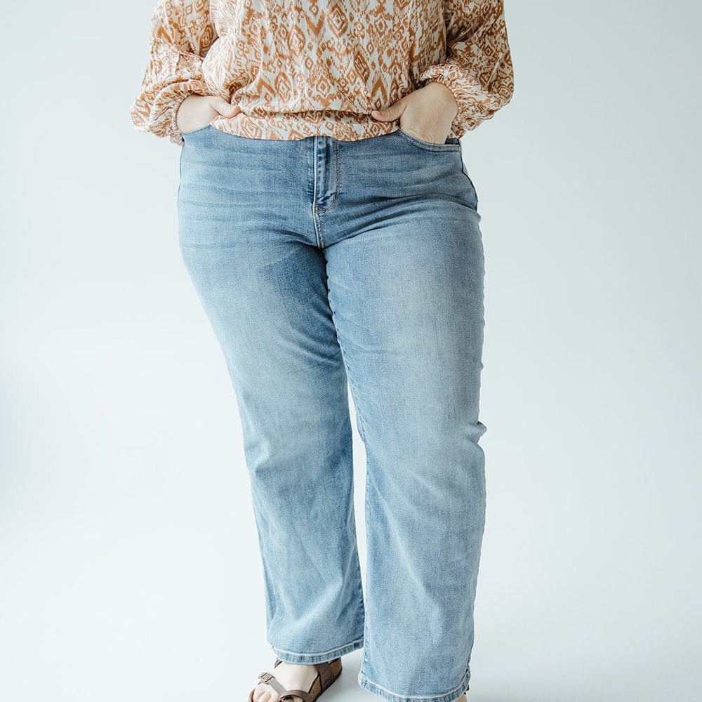 Person wearing a patterned top, JUDY BLUE HIGH WAIST NON-DISTRESSED STRAIGHT LEG JEAN by Judy Blue, and sandals stands with hands in pockets against a plain background.