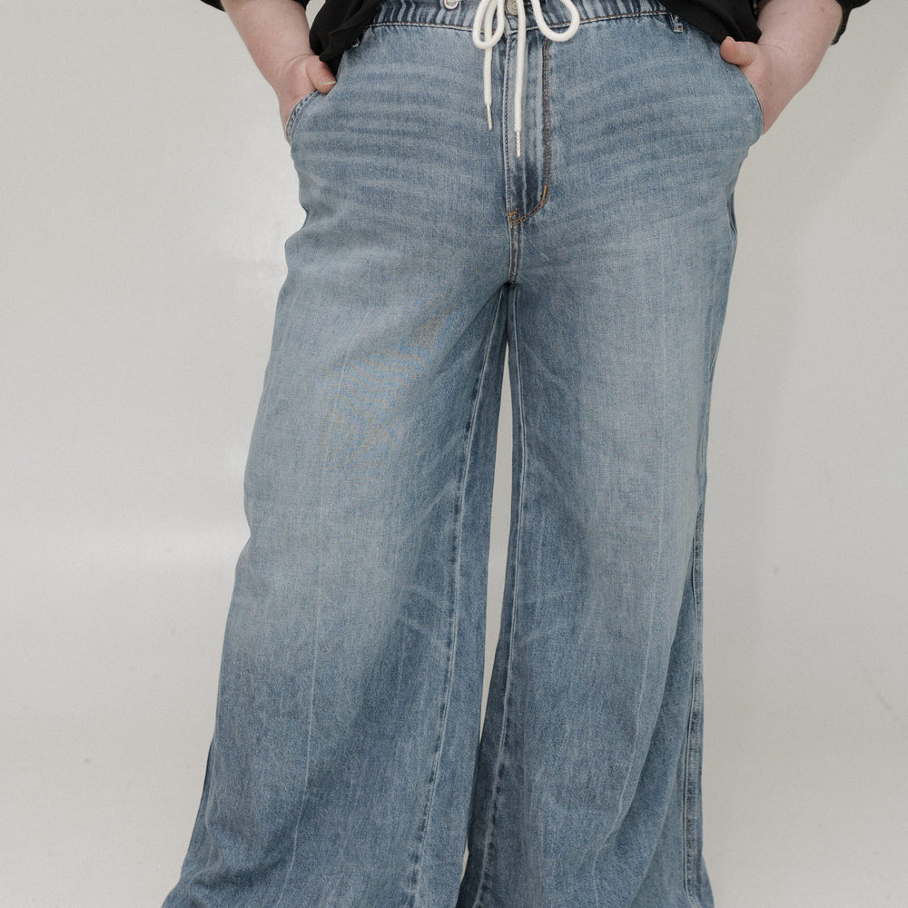 Person wearing wide-leg blue jeans and a black top on a white background