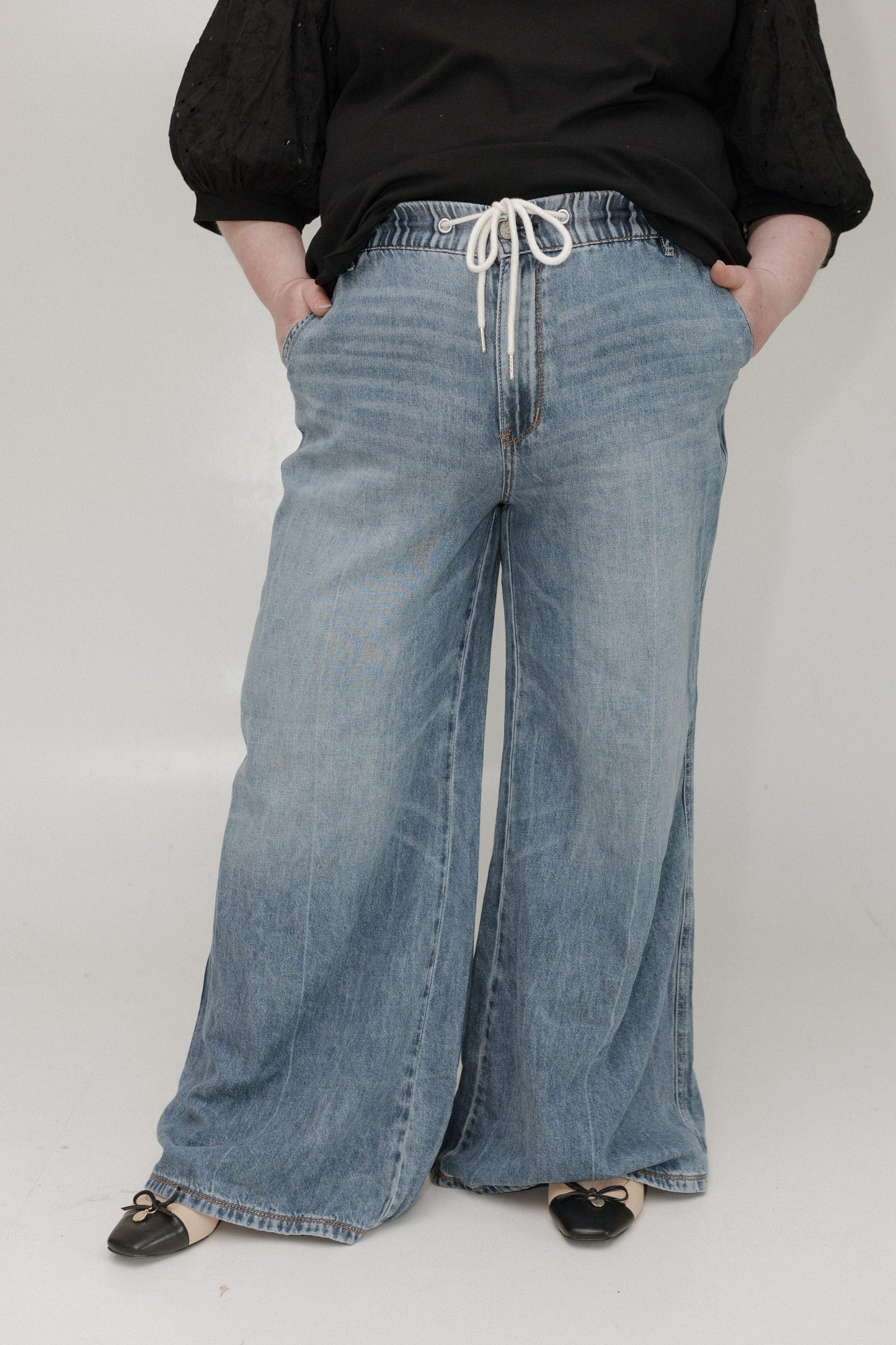 Person wearing wide-leg blue jeans and a black top on a white background