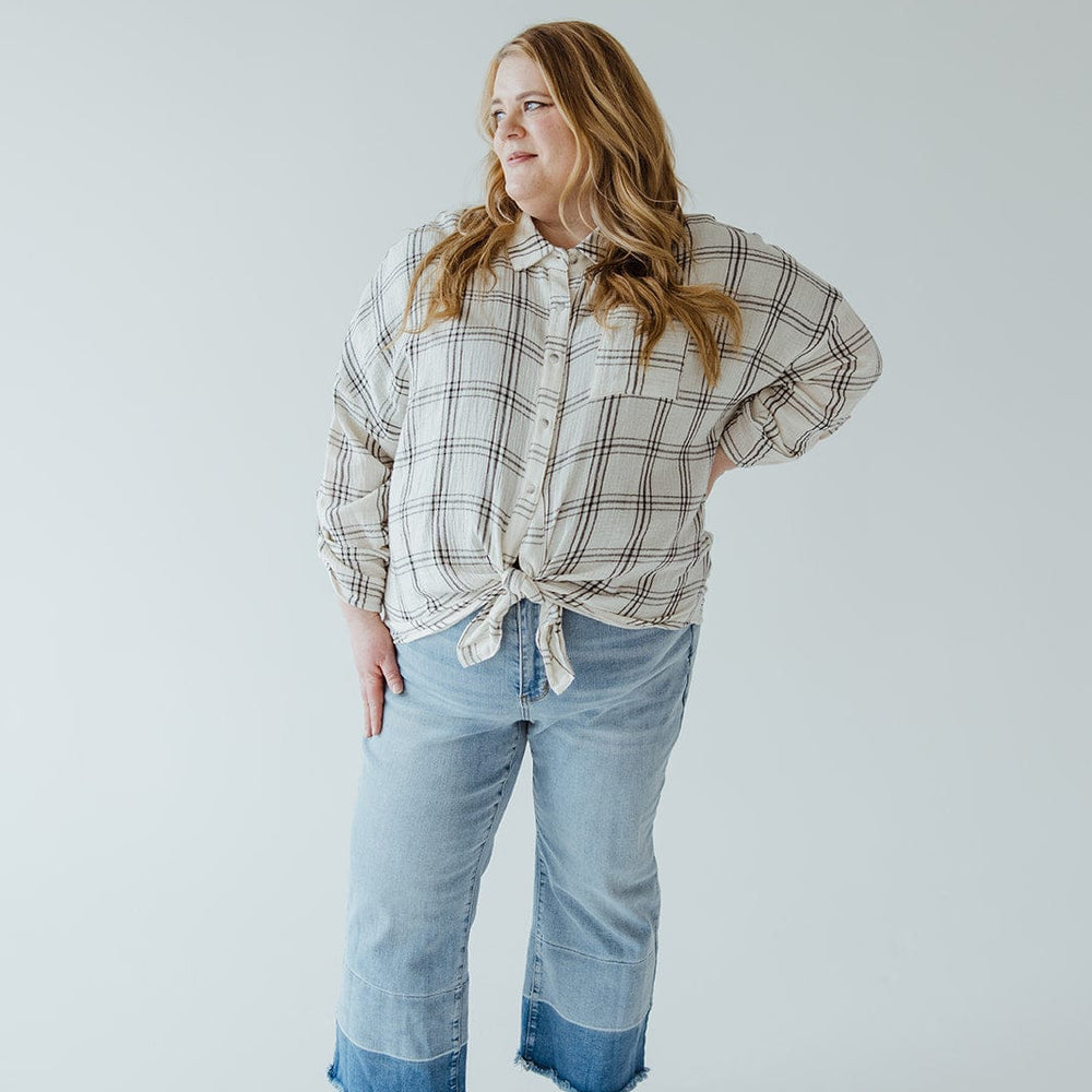 A woman stands with one hand on her hip, wearing a plaid shirt, Judy Blue JUDY BLUE HIGH WAIST RELEASED HEM CROPPED WIDE LEG jeans with rolled cuffs, and black sandals, against a plain background.