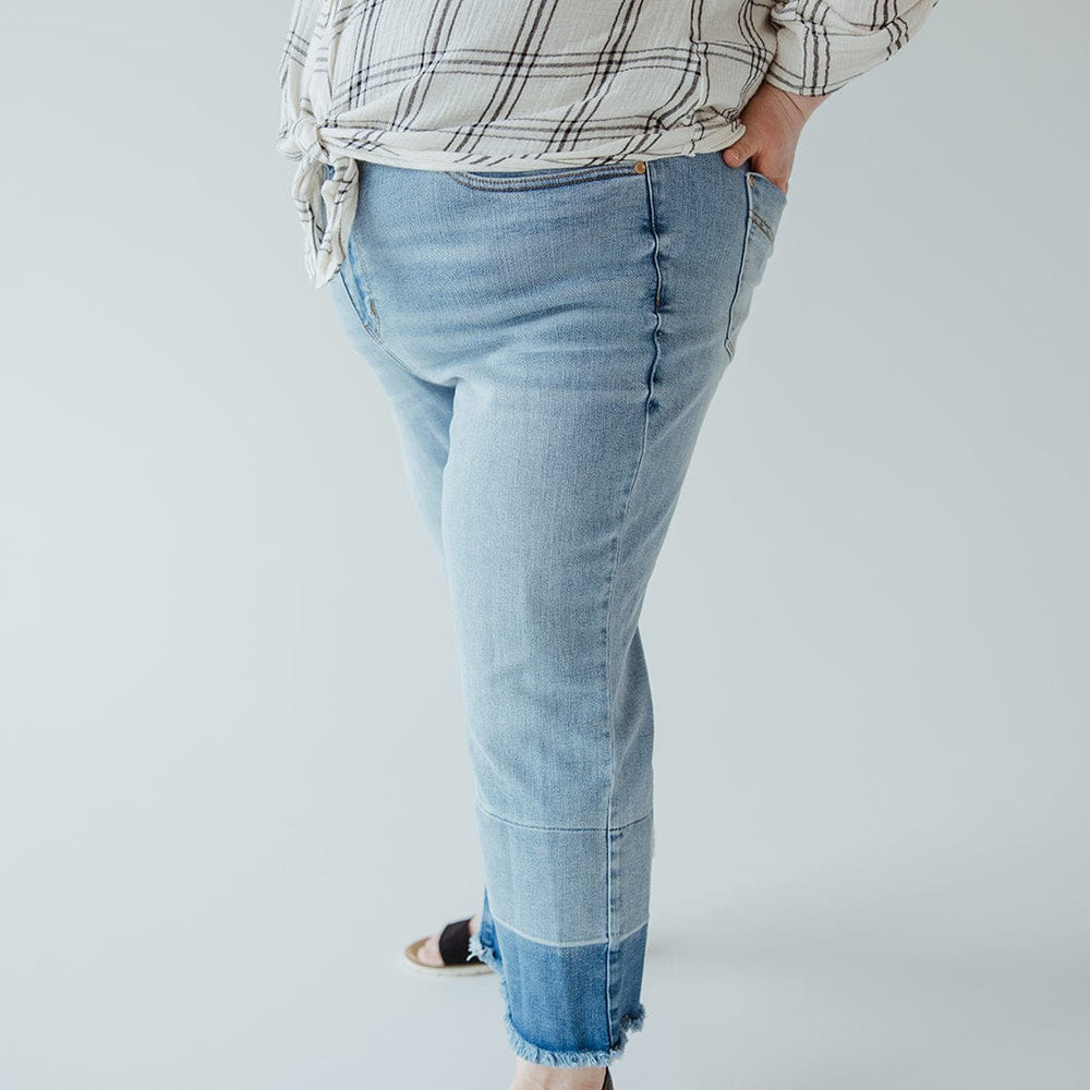 A person is wearing a plaid shirt, light blue Judy Blue JUDY BLUE HIGH WAIST RELEASED HEM CROPPED WIDE LEG jeans, and black sandals, with hands in pockets. The image is cropped above the shoulders, showing only the torso and legs.