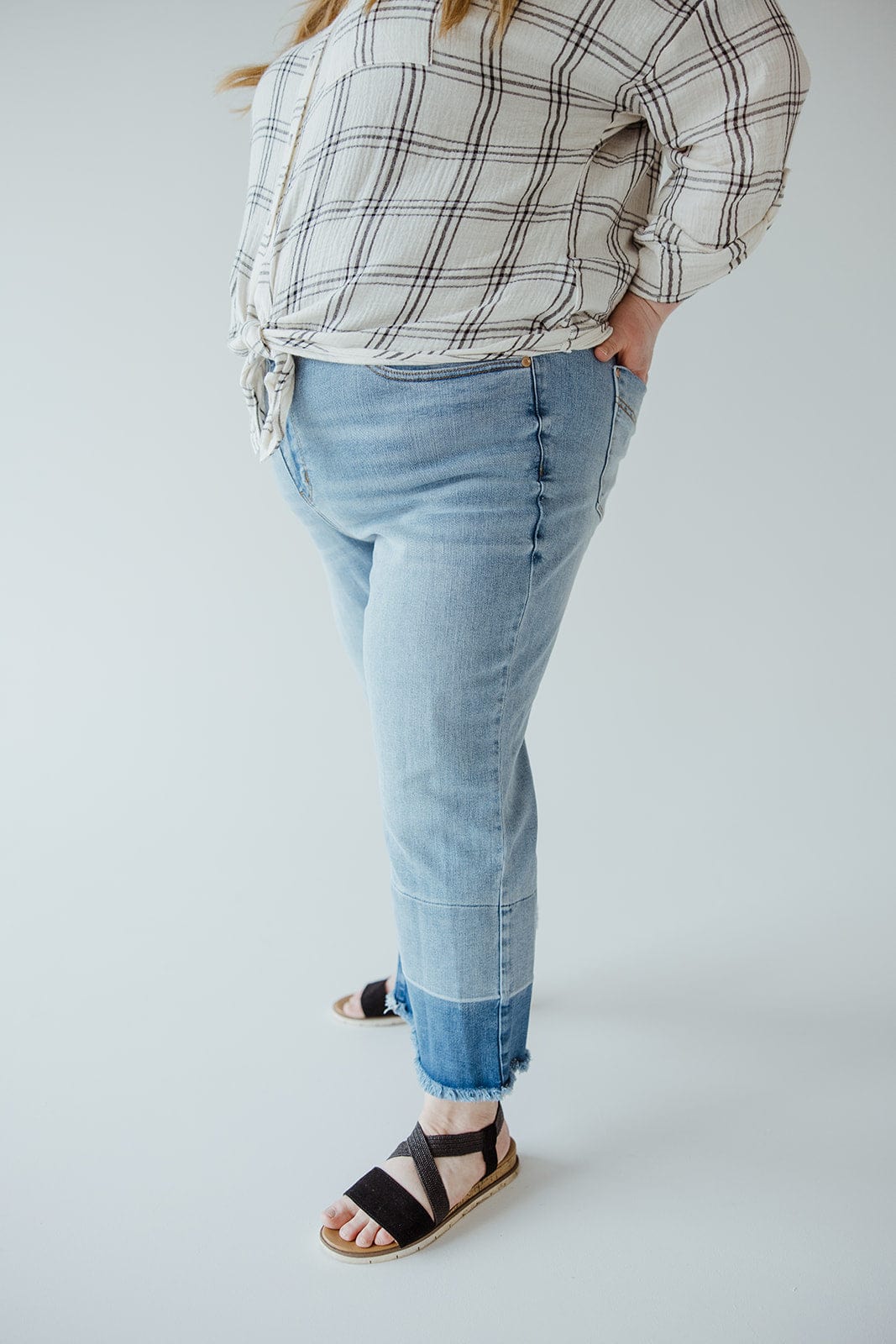 A person is wearing a plaid shirt, light blue Judy Blue JUDY BLUE HIGH WAIST RELEASED HEM CROPPED WIDE LEG jeans, and black sandals, with hands in pockets. The image is cropped above the shoulders, showing only the torso and legs.