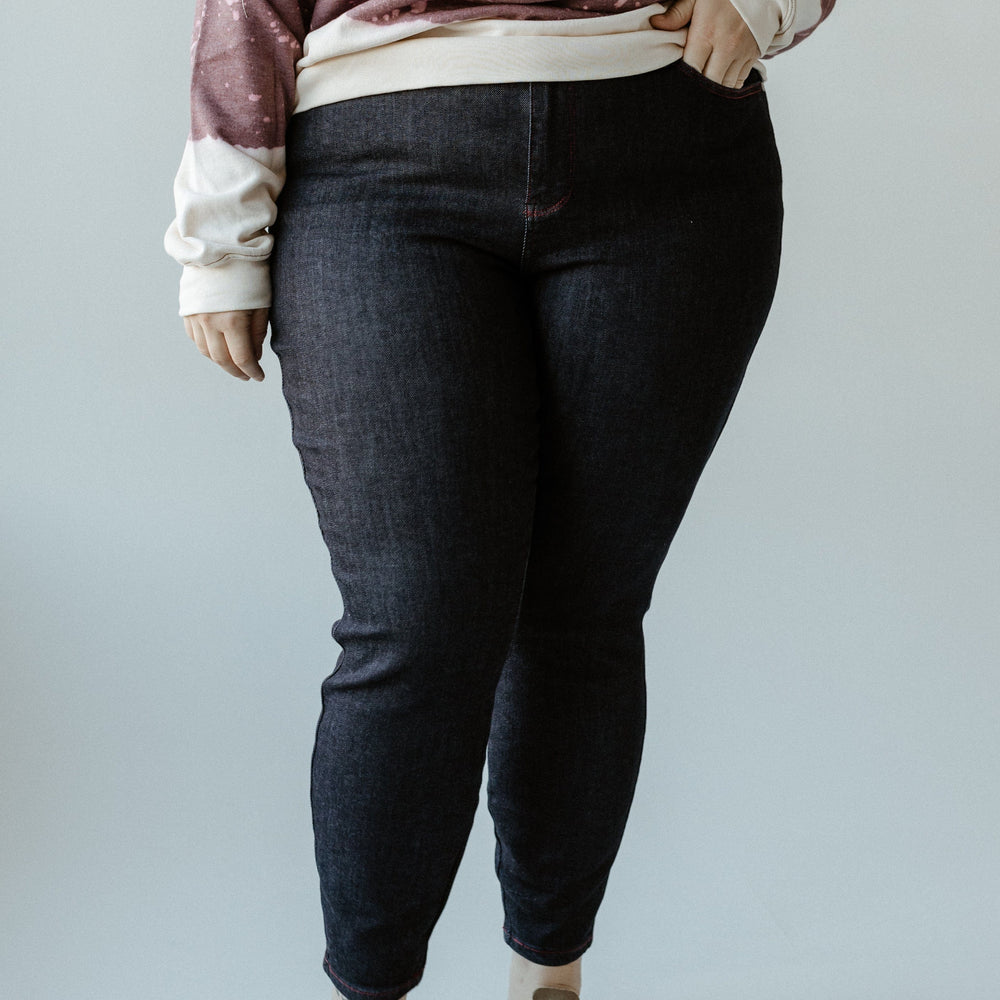 A person wearing a purple sweatshirt that reads "The Bunch of Crazies" pairs it with dark denim high-waist skinny jeans, featuring heart-shaped back pockets, and beige shoes. They stand confidently against a plain background, showcasing their unique style.