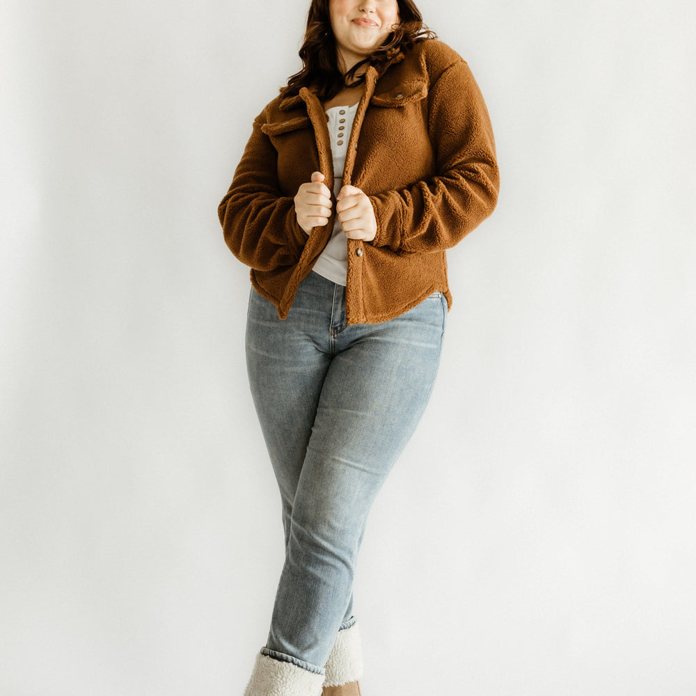 Person wearing a brown jacket, medium wash jeans, and beige boots poses gracefully against a plain white background, showcasing the flattering fit of high waist straight leg jeans.