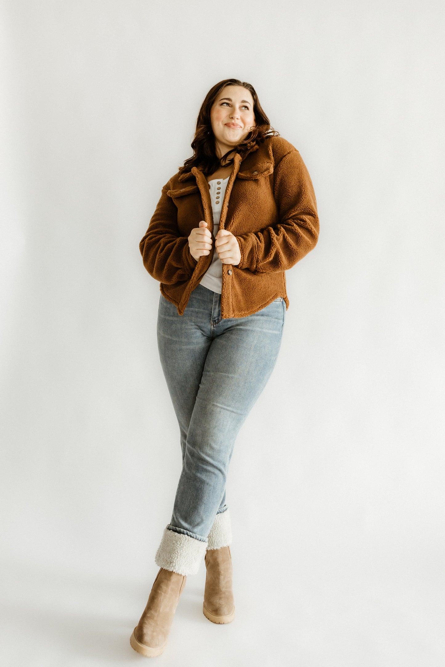 Person wearing a brown jacket, medium wash jeans, and beige boots poses gracefully against a plain white background, showcasing the flattering fit of high waist straight leg jeans.