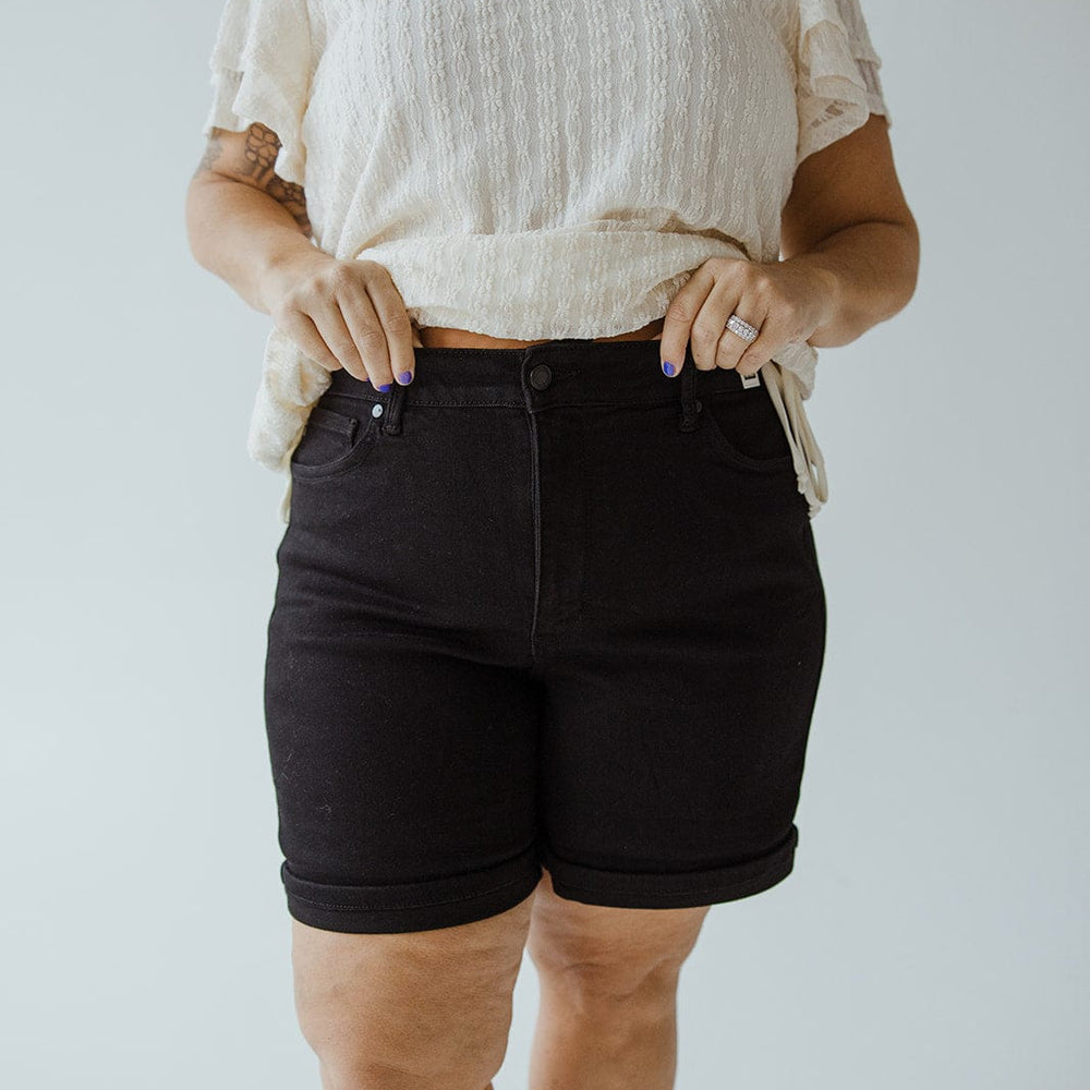 A person wearing a white blouse and Judy Blue JUDY BLUE HIGH WAIST TUMMY CONTROL CUFFED SHORTS IN BLACK poses against a plain background.