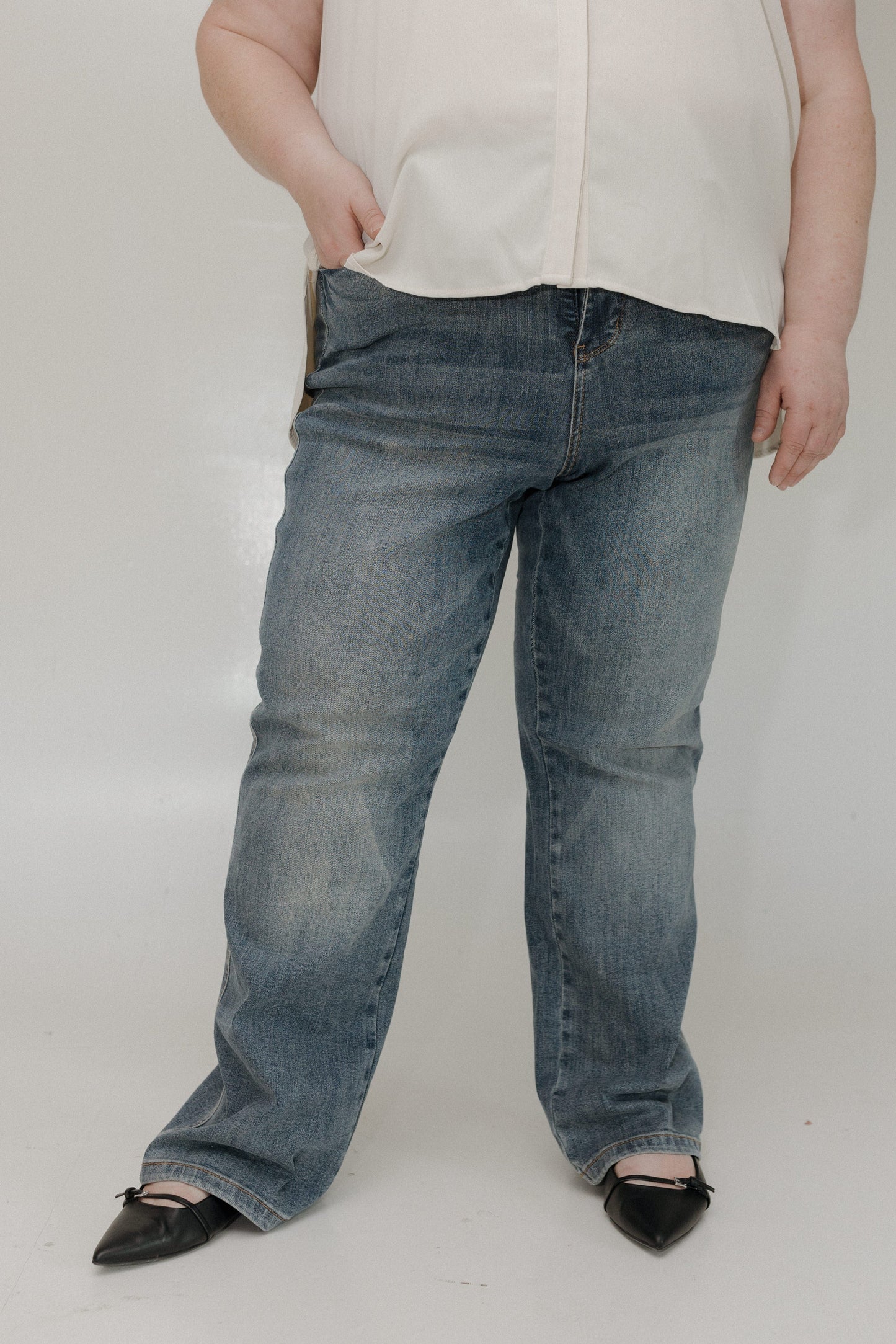 Person wearing blue jeans and a white shirt on a plain background