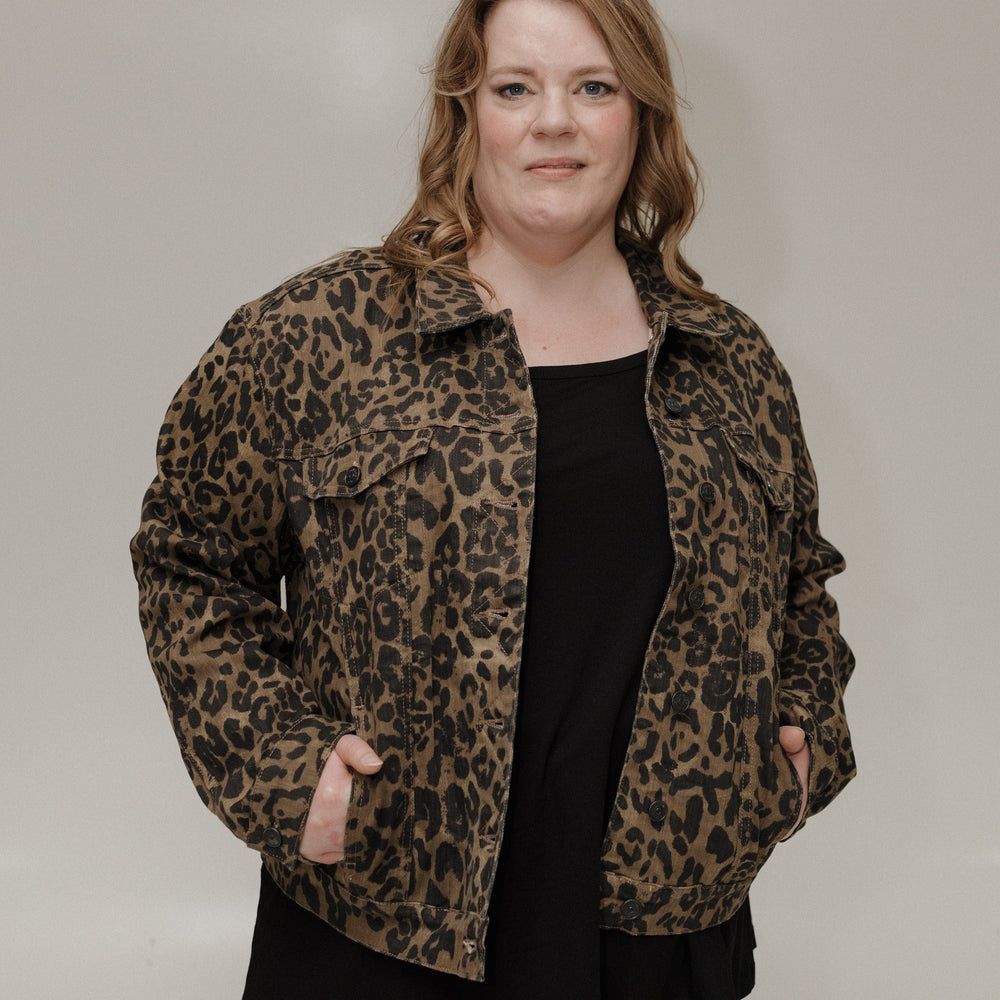 Person wearing a leopard print jacket over a black top and white pants on a plain background