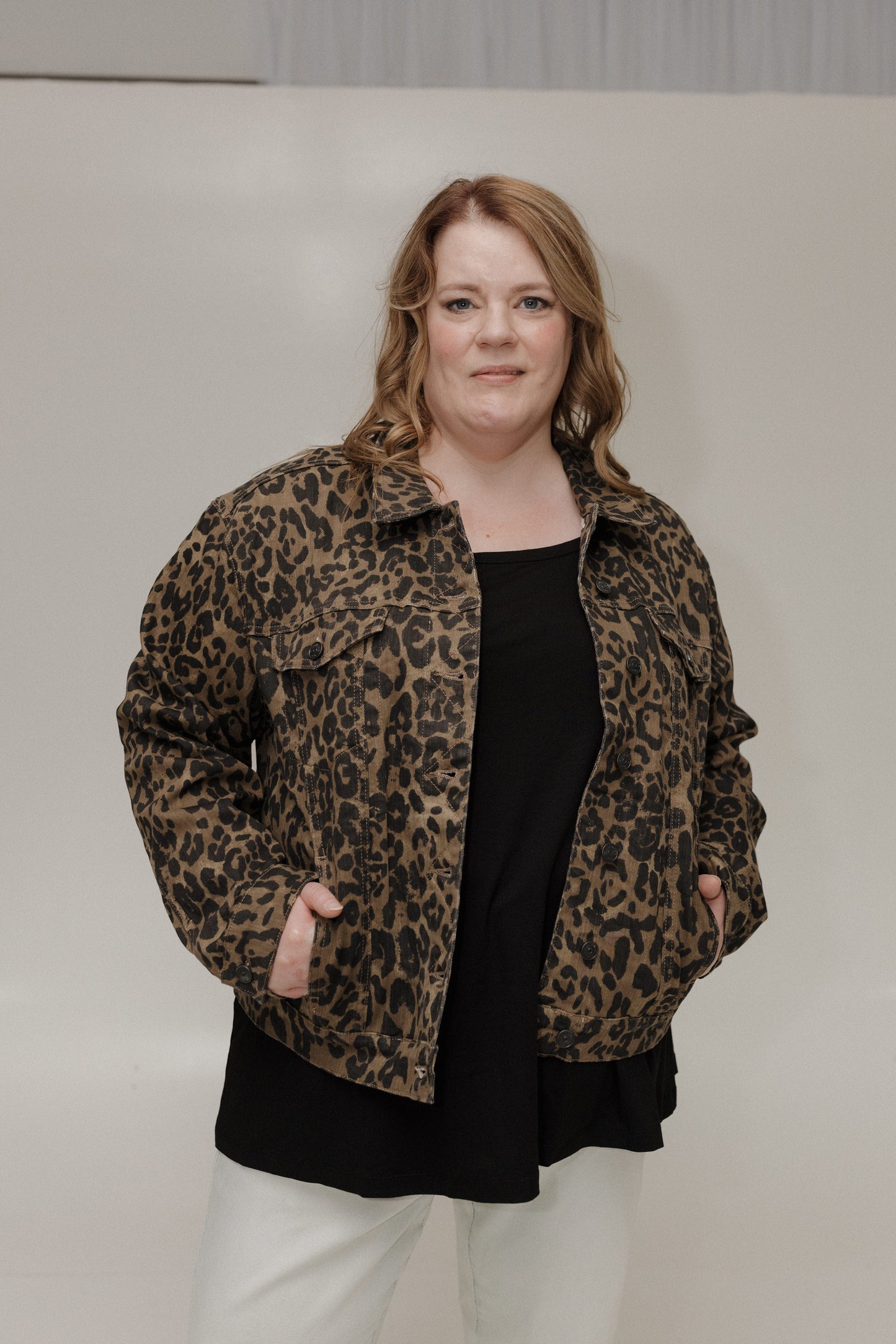 Person wearing a leopard print jacket over a black top and white pants on a plain background
