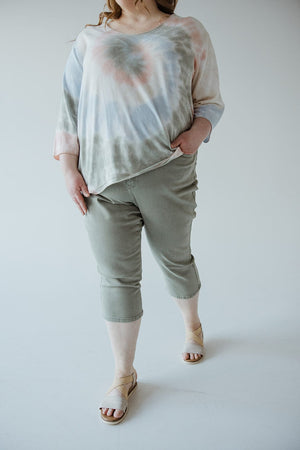 A person is wearing a pastel tie-dye shirt, Judy Blue Mid-Rise Non-Distressed Capris in Sage by Judy Blue, and beige sandals. The person's left hand is in their pocket.