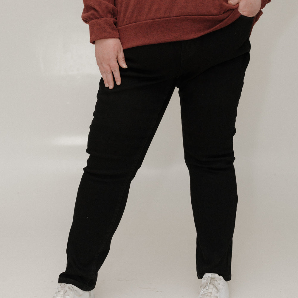 Person wearing a brown sweatshirt, black pants, and white sneakers on a plain background