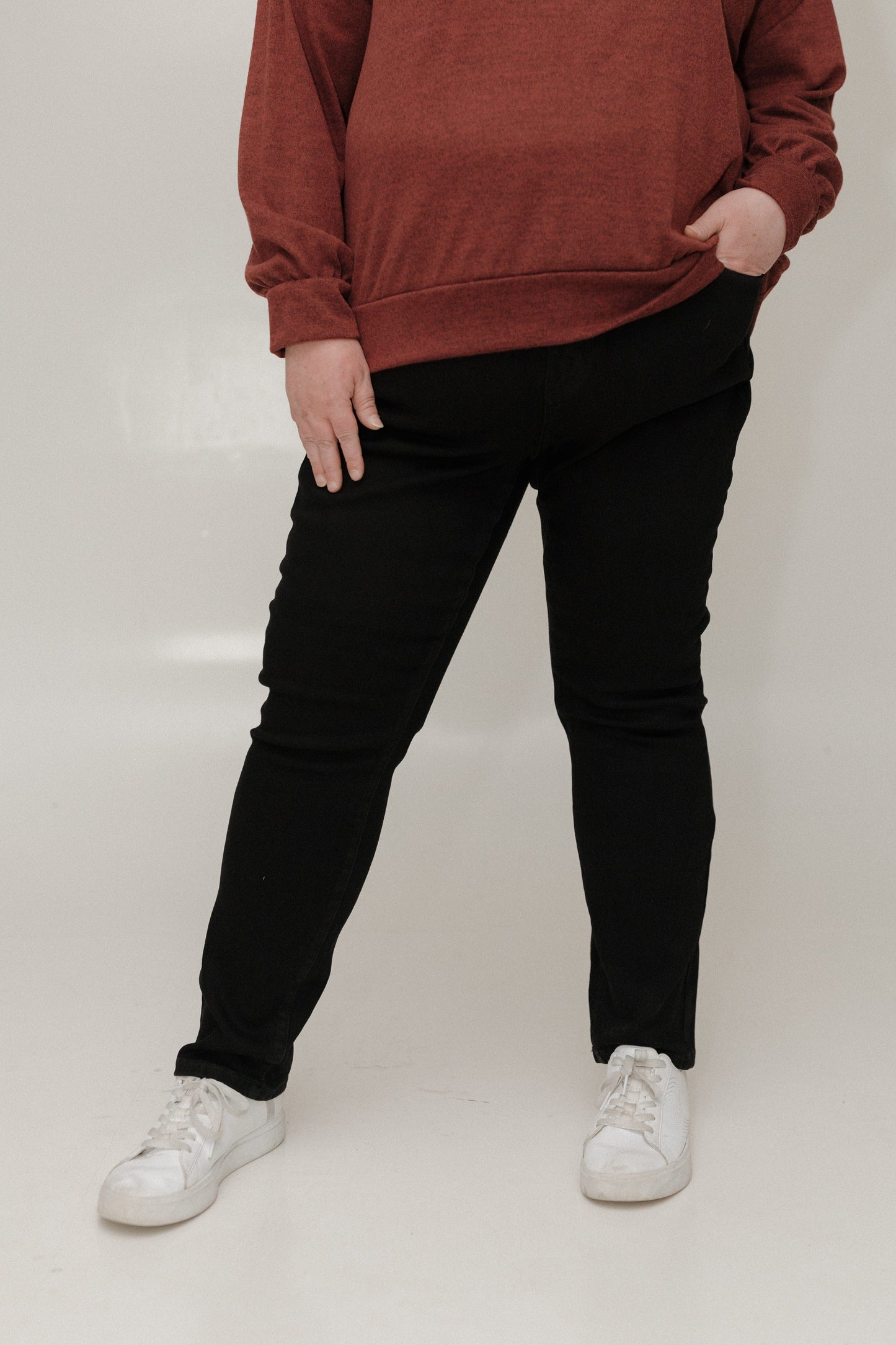 Person wearing a brown sweatshirt, black pants, and white sneakers on a plain background