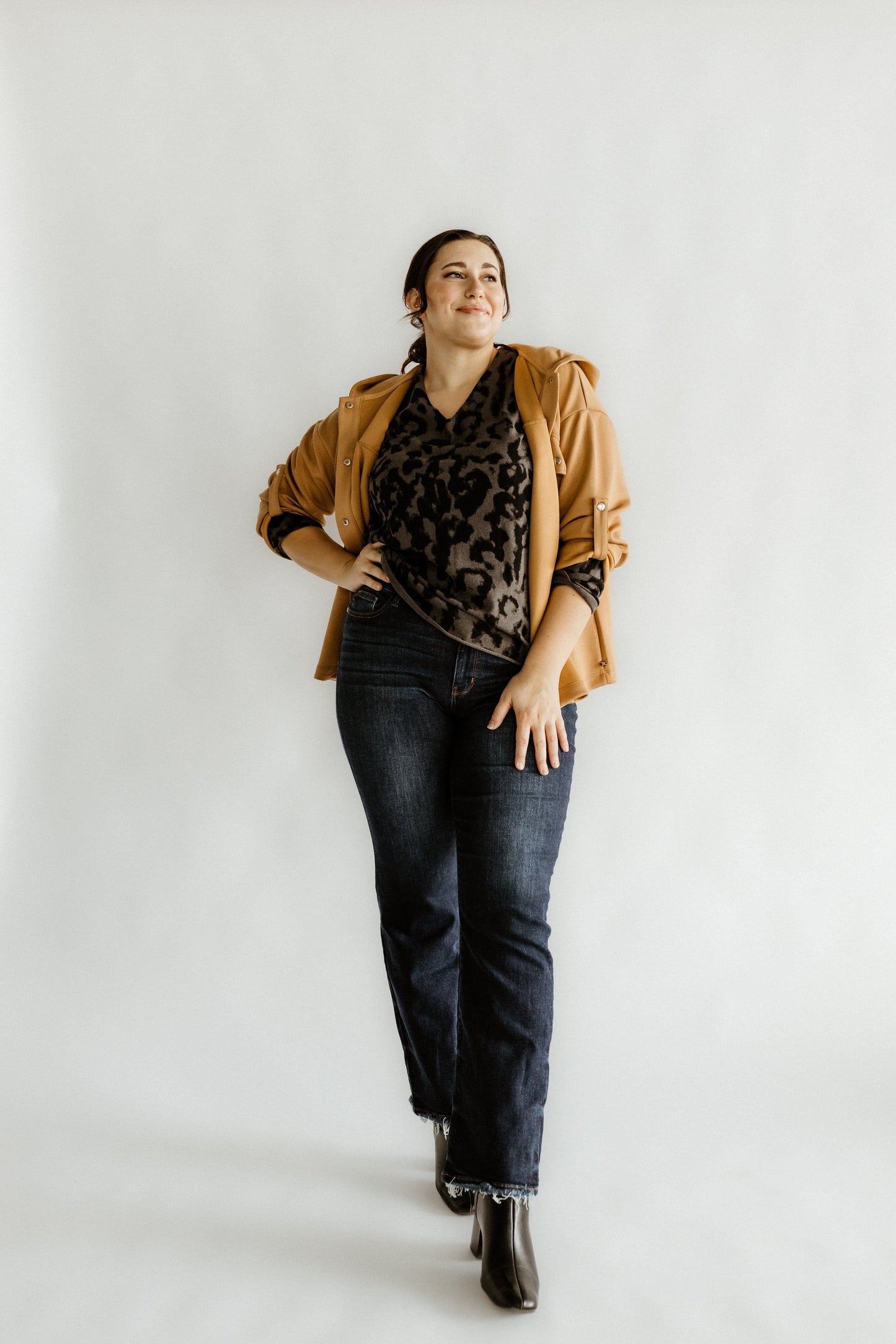 Person posing confidently in a leopard print top, brown jacket, and Judy Blue mid-rise straight leg jeans paired with black boots against a plain background.