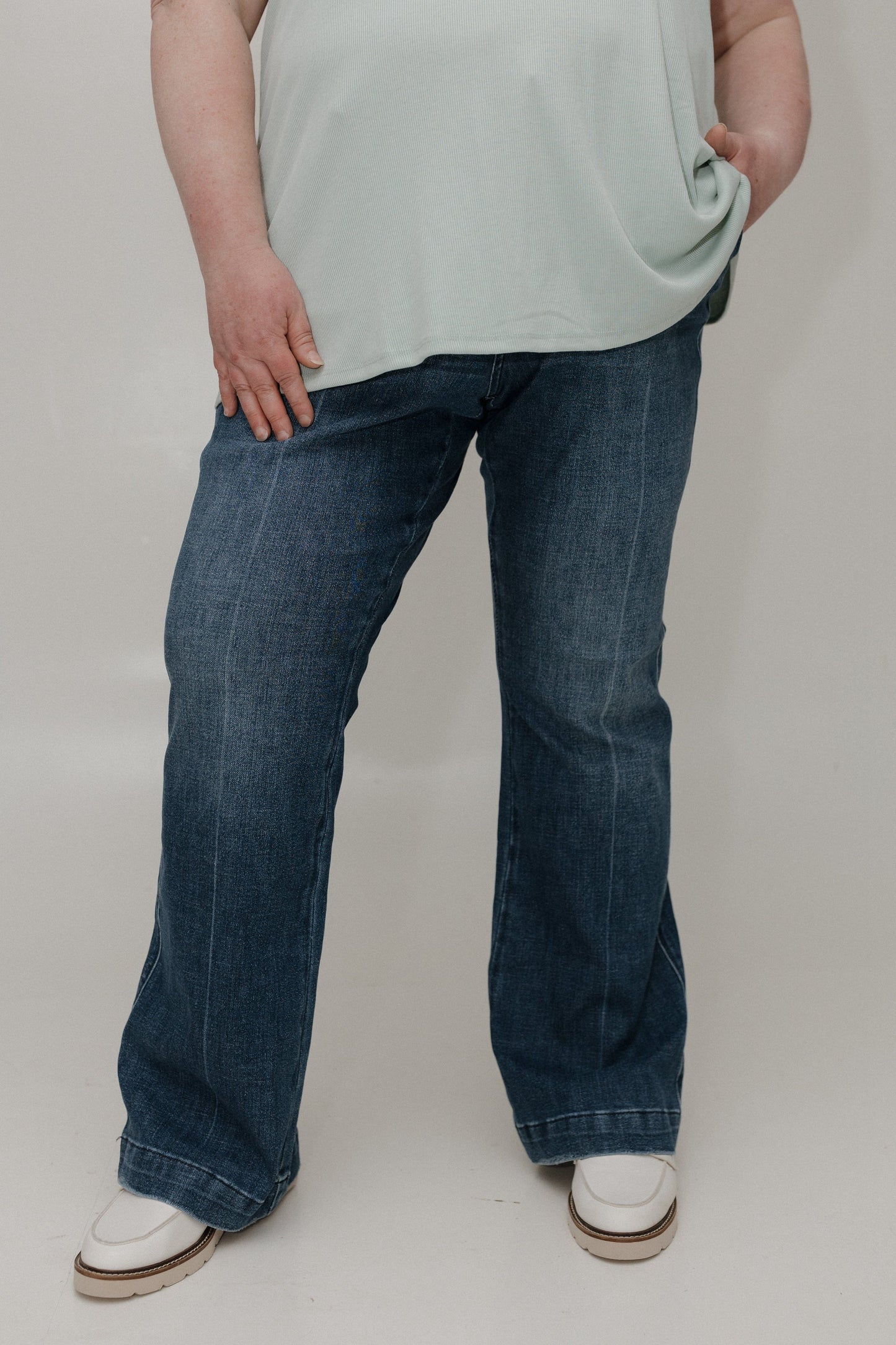 Person wearing blue jeans and a light-colored shirt on a plain background