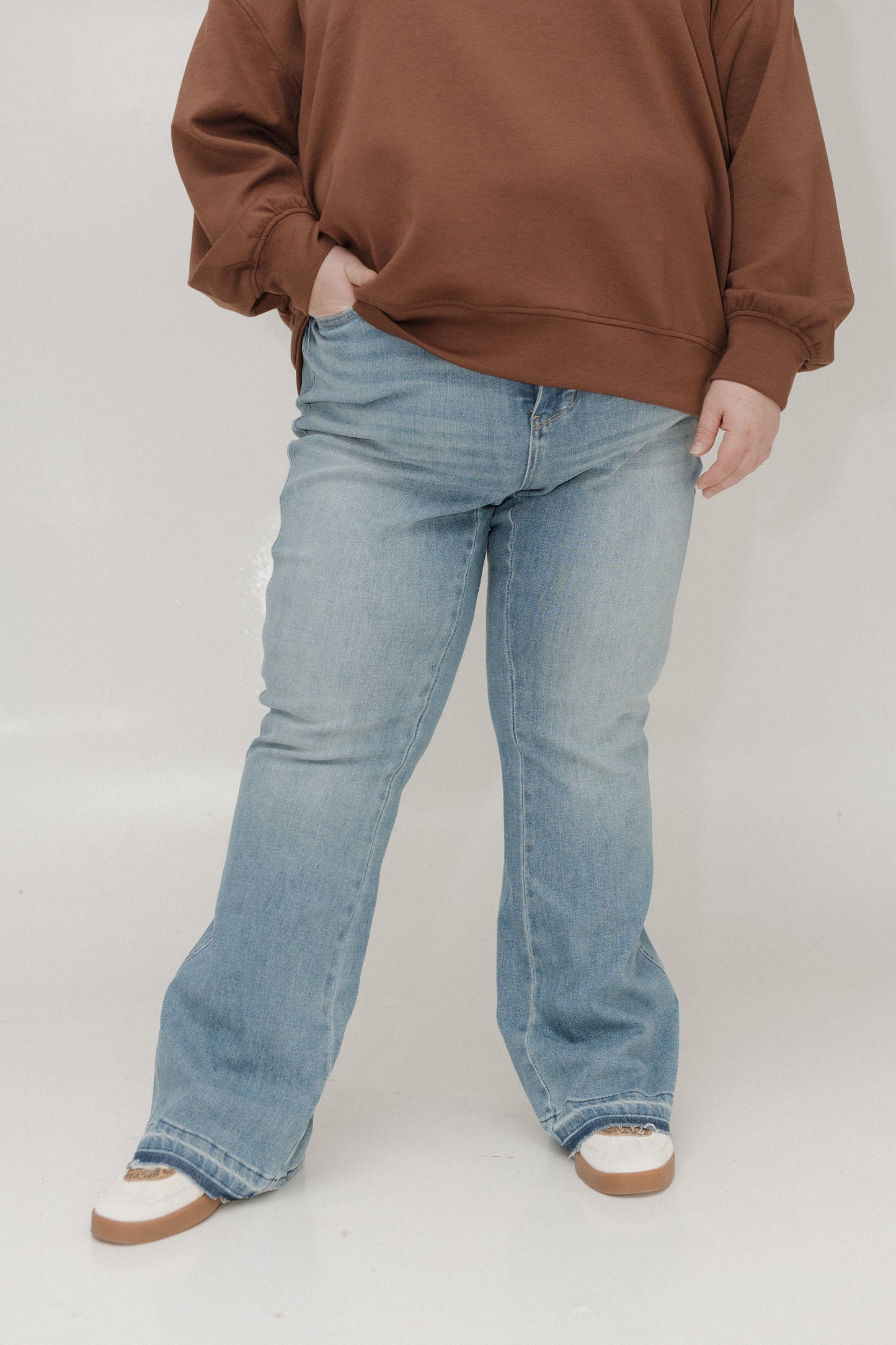 Person wearing a brown sweatshirt and light blue jeans on a white background