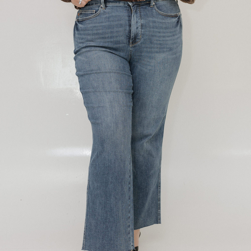 Person wearing blue jeans and a brown distressed top on a white background