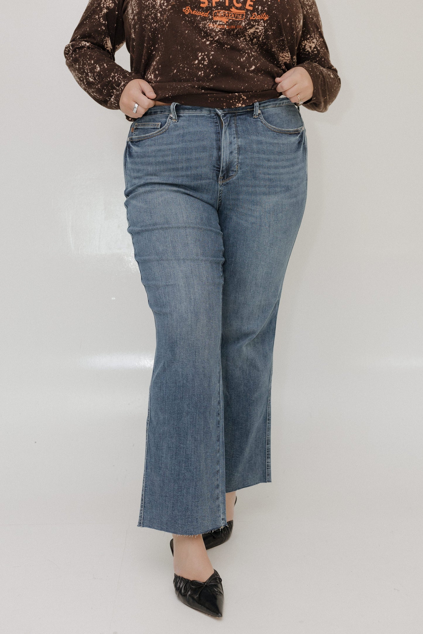 Person wearing blue jeans and a brown distressed top on a white background