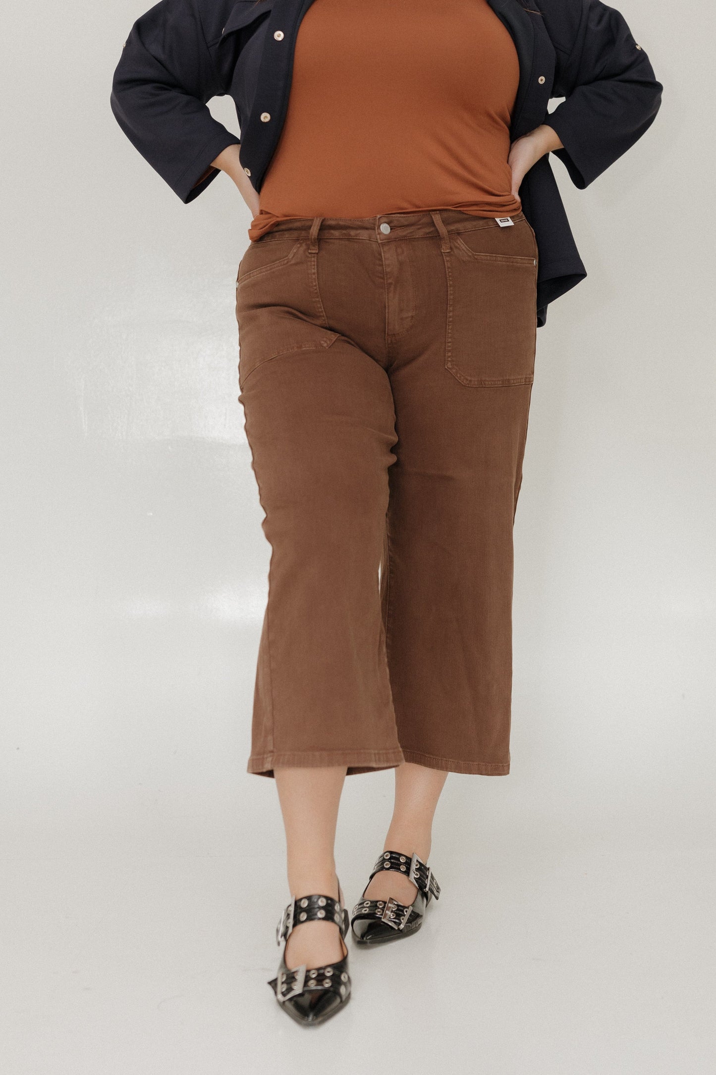 Person wearing a brown top and pants with a black jacket on a white background