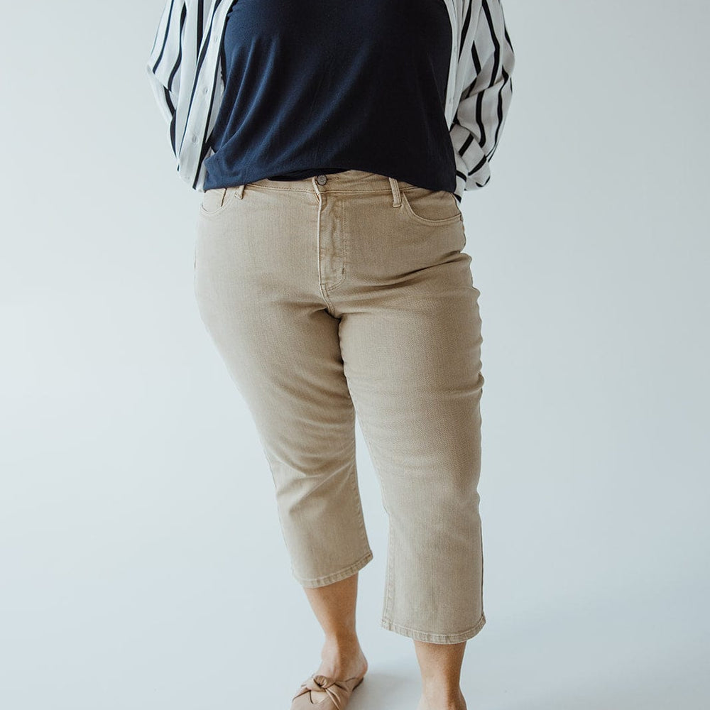 A person wearing a black top, black and white striped jacket, Judy Blue JUDY BLUE NON-DISTRESSED CAPRI IN WASHED KHAKI, and beige shoes stands against a plain background, showcasing an effortlessly chic summer style.