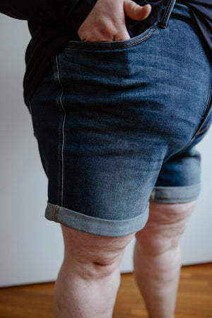 A person wearing a black shirt and Judy Blue JUDY BLUE TUMMY CONTROL CUFFED SHORTS IN VINTAGE WASH with their right hand in their pocket.