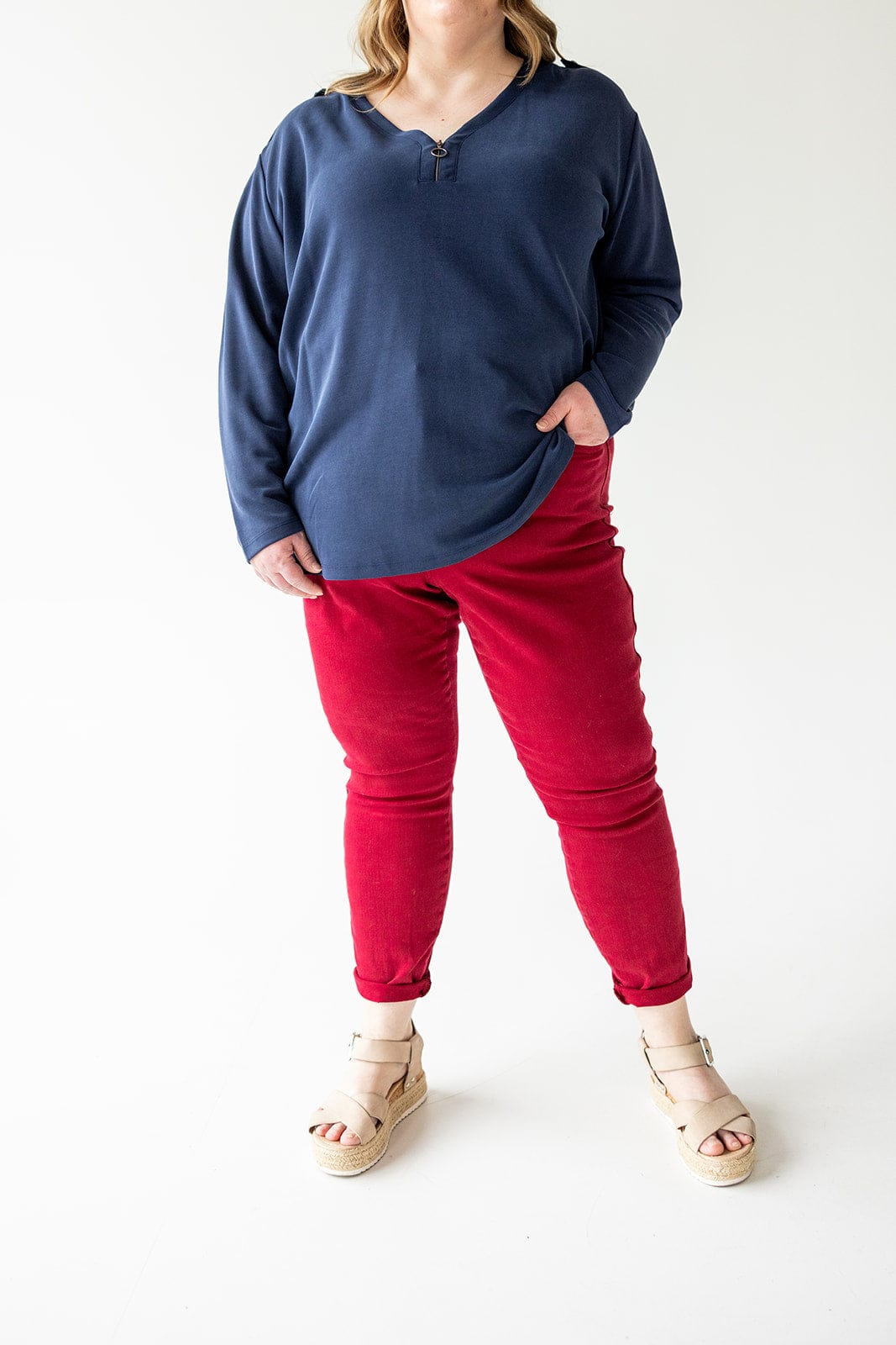 Person wearing a long-sleeve navy blue shirt, Judy Blue Tummy Control Skinny Jeans in Scarlet, and beige sandals, standing against a plain white background. Face is not visible.