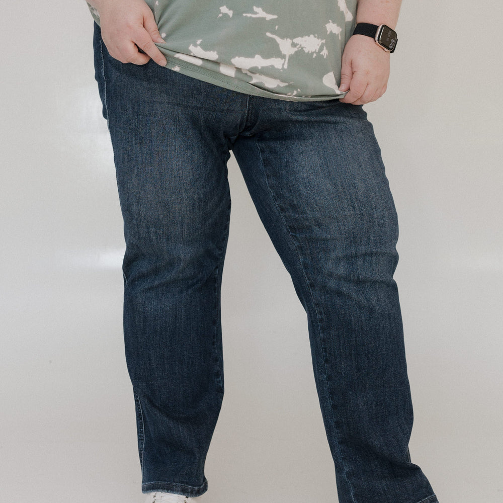 Person wearing a camouflage shirt, blue jeans, and white sneakers on a plain background