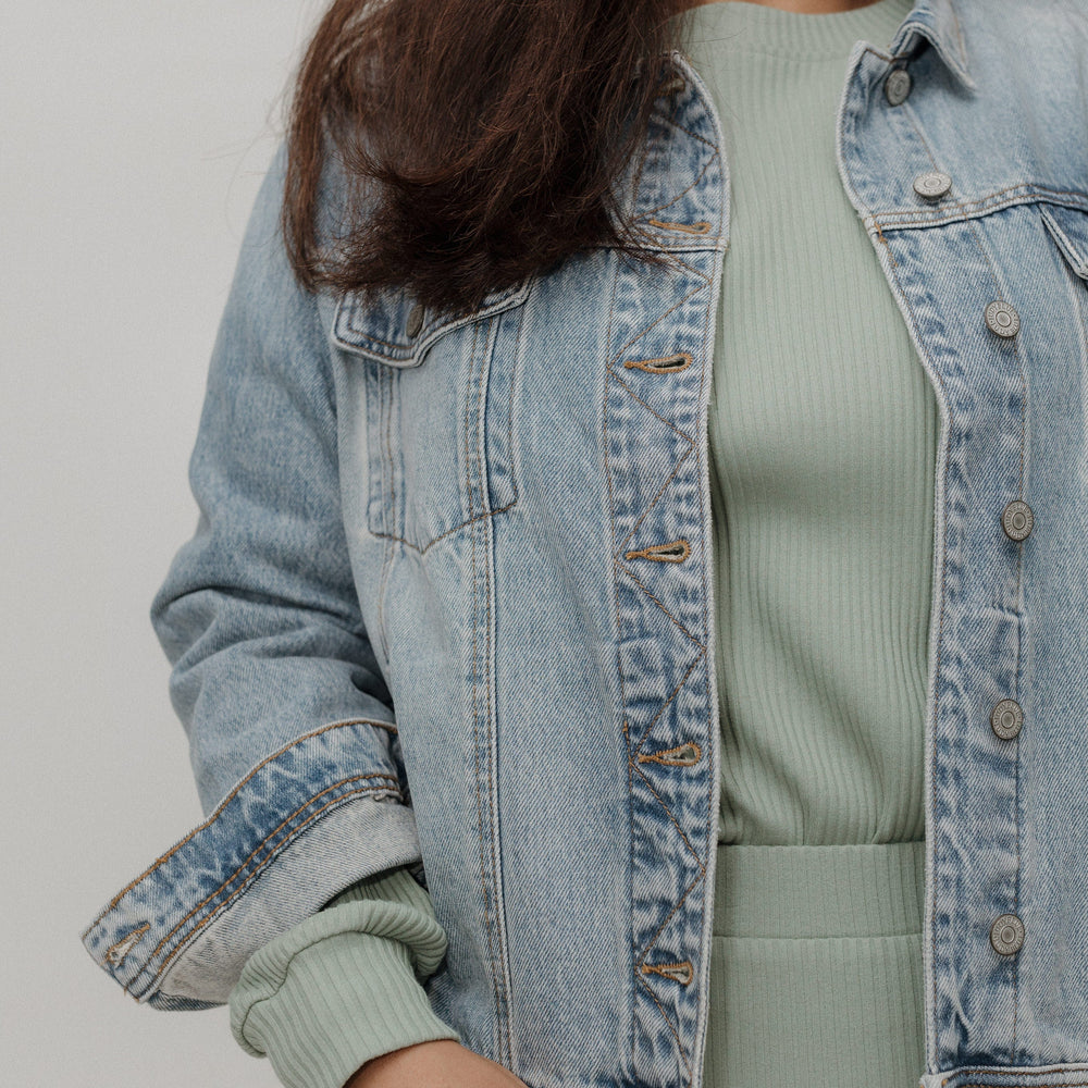 Person wearing a light blue denim jacket over a green outfit on a plain background