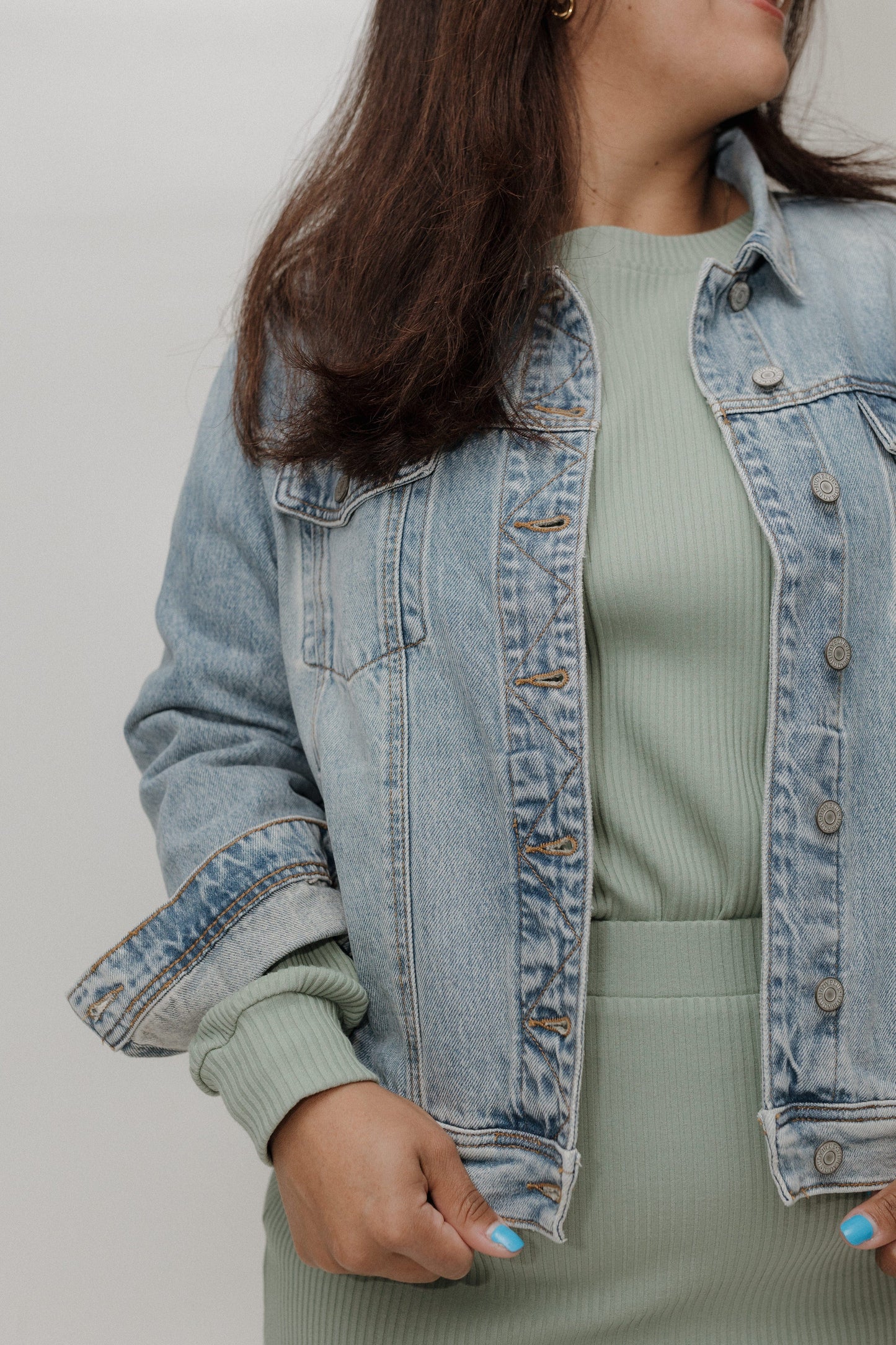 Person wearing a light blue denim jacket over a green outfit on a plain background