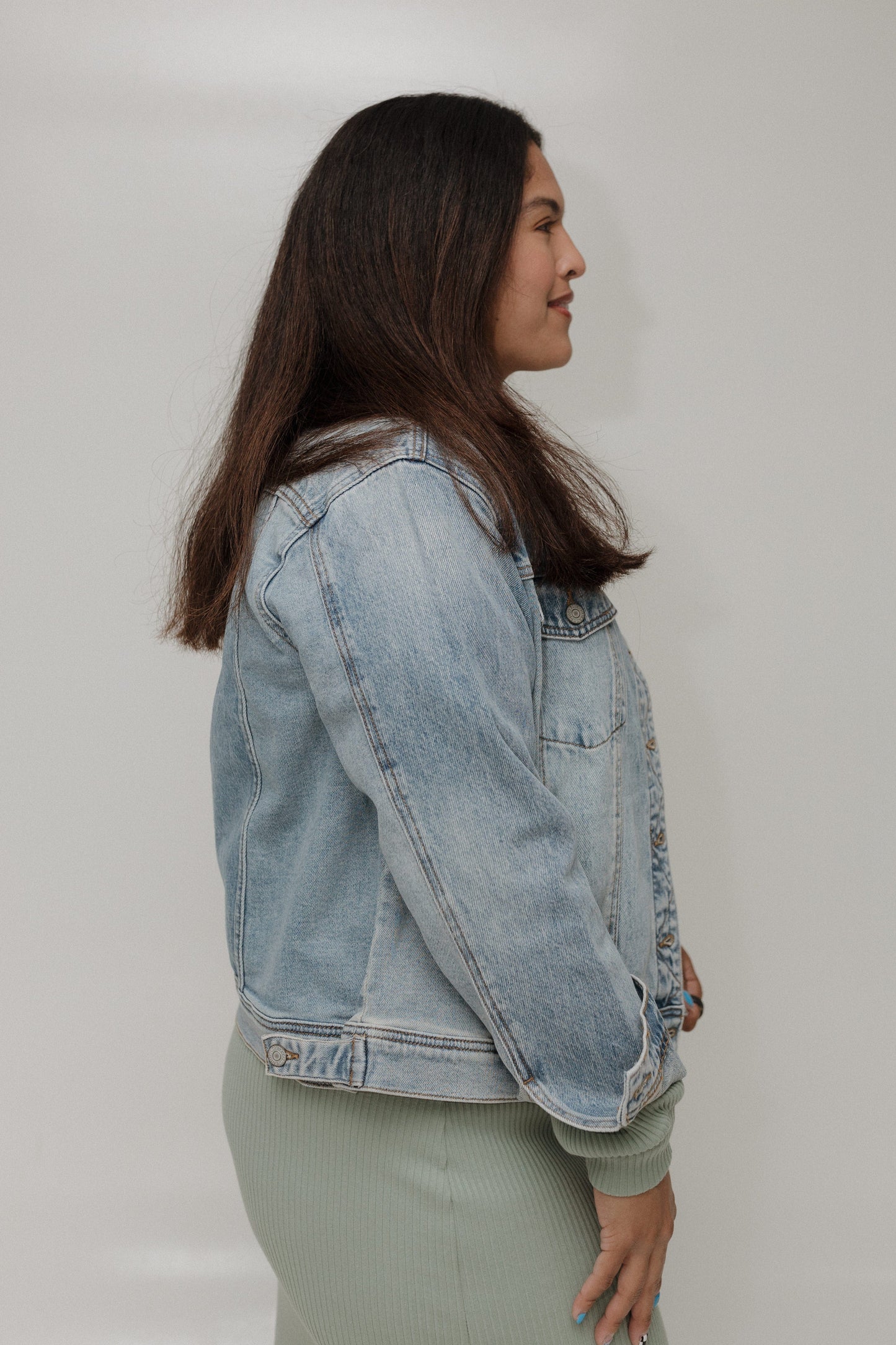 Woman wearing a light blue denim jacket against a plain background