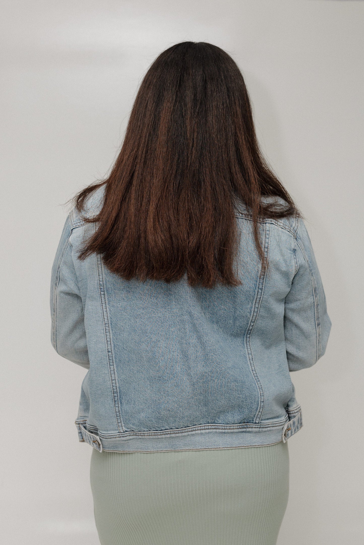 Person wearing a light blue denim jacket from behind on a plain background