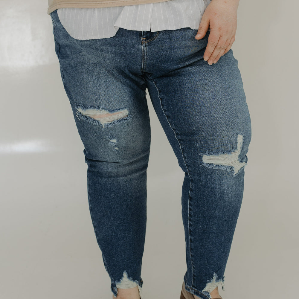 Person wearing distressed blue jeans and a beige sweater on a plain background
