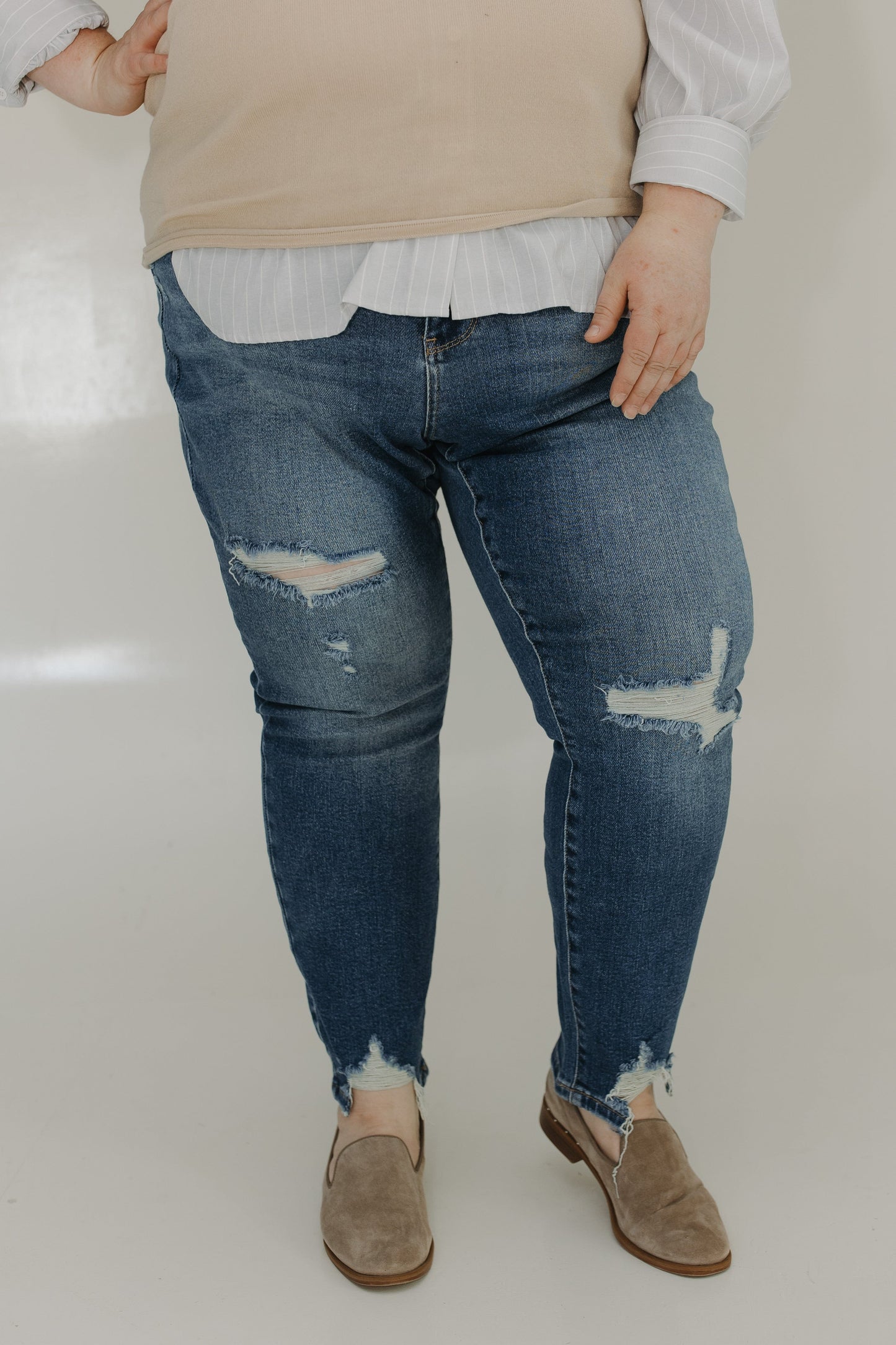 Person wearing distressed blue jeans and a beige sweater on a plain background