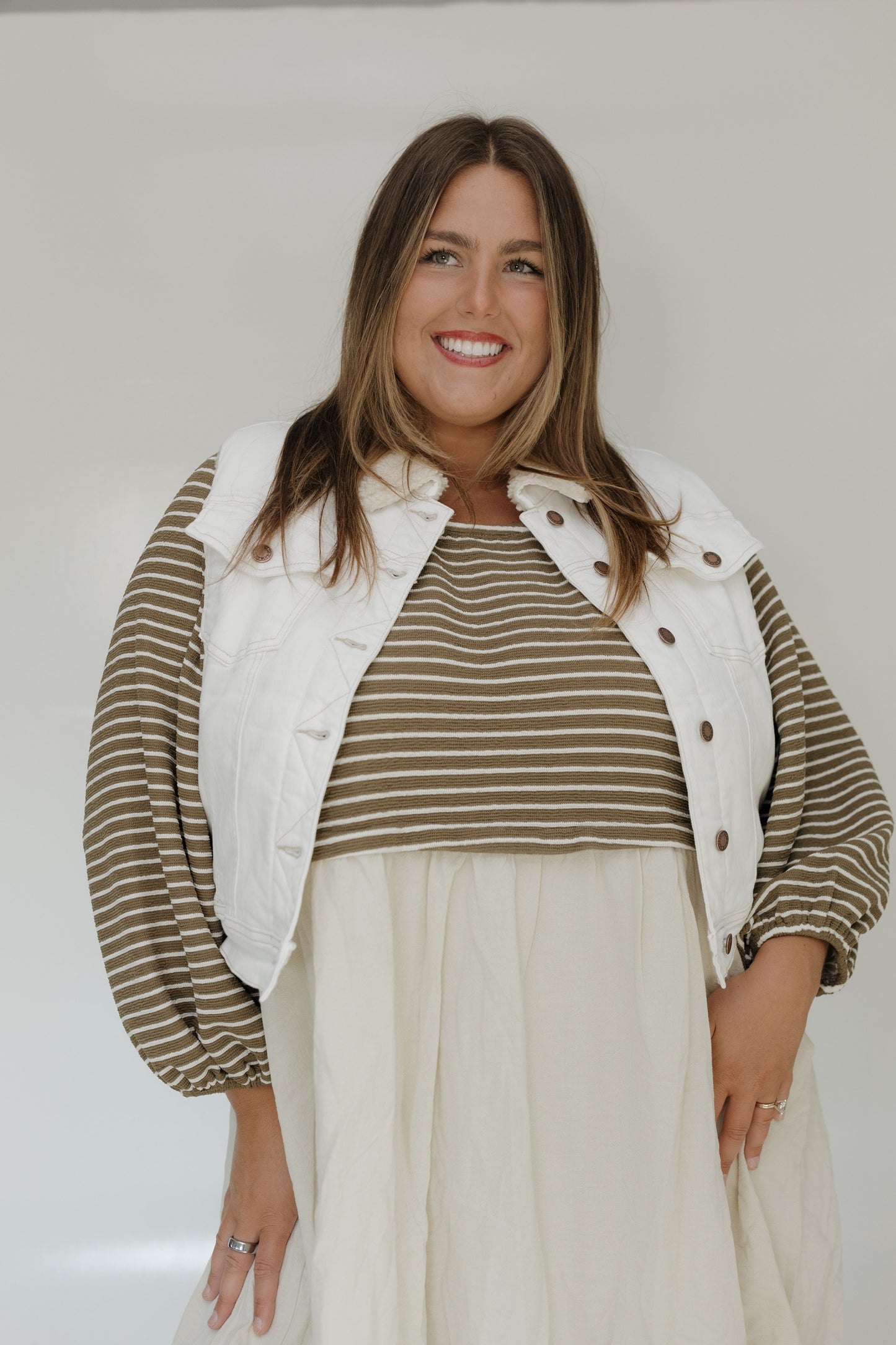 Woman wearing a striped shirt and white vest against a plain background