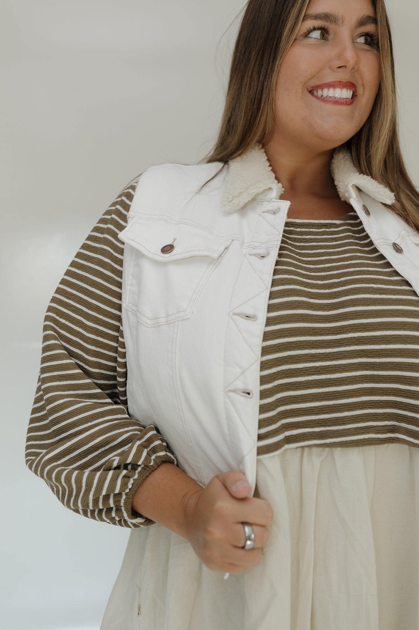 Woman wearing a white denim vest over a striped shirt with a neutral background