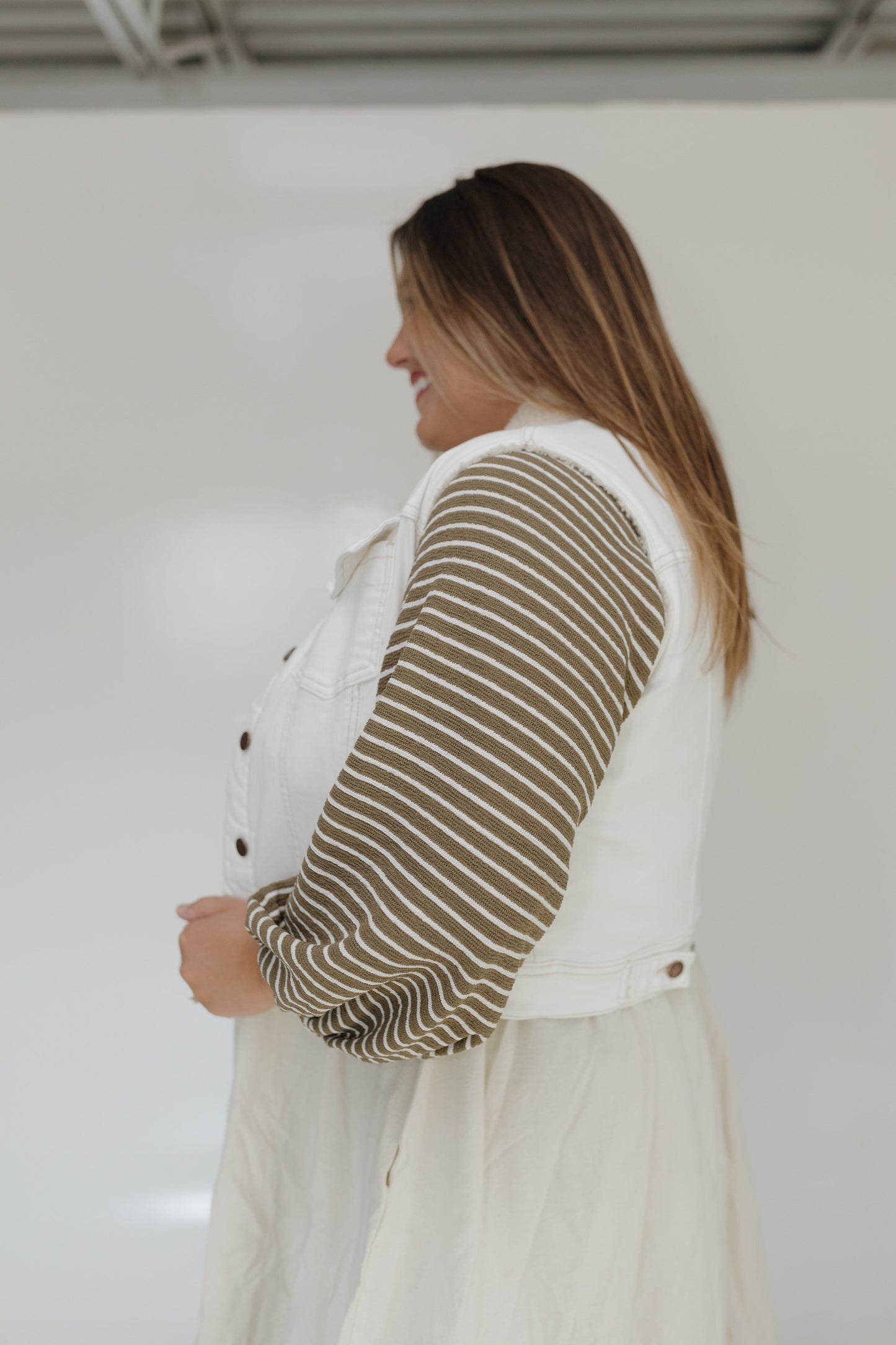 Woman wearing a white outfit with a striped sleeve against a plain background