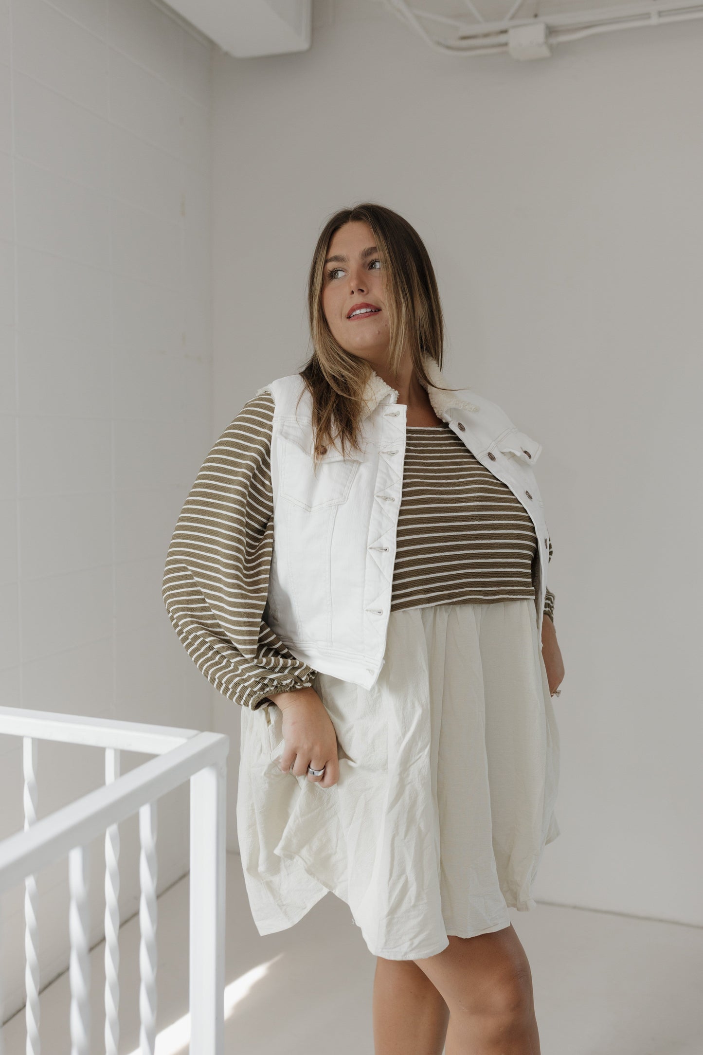 Woman wearing a white vest over a striped shirt with a plain background