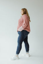 A person with long hair, wearing a pink sweater, Judy Blue High-Waisted Non-Distressed Skinny Jean in Dark Wash, and white sneakers stands facing away from the camera against a plain background.