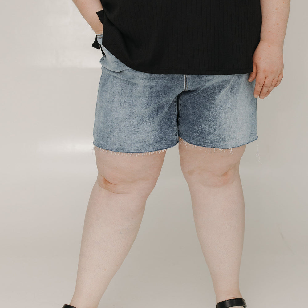 Person wearing black t-shirt and denim shorts on a plain background