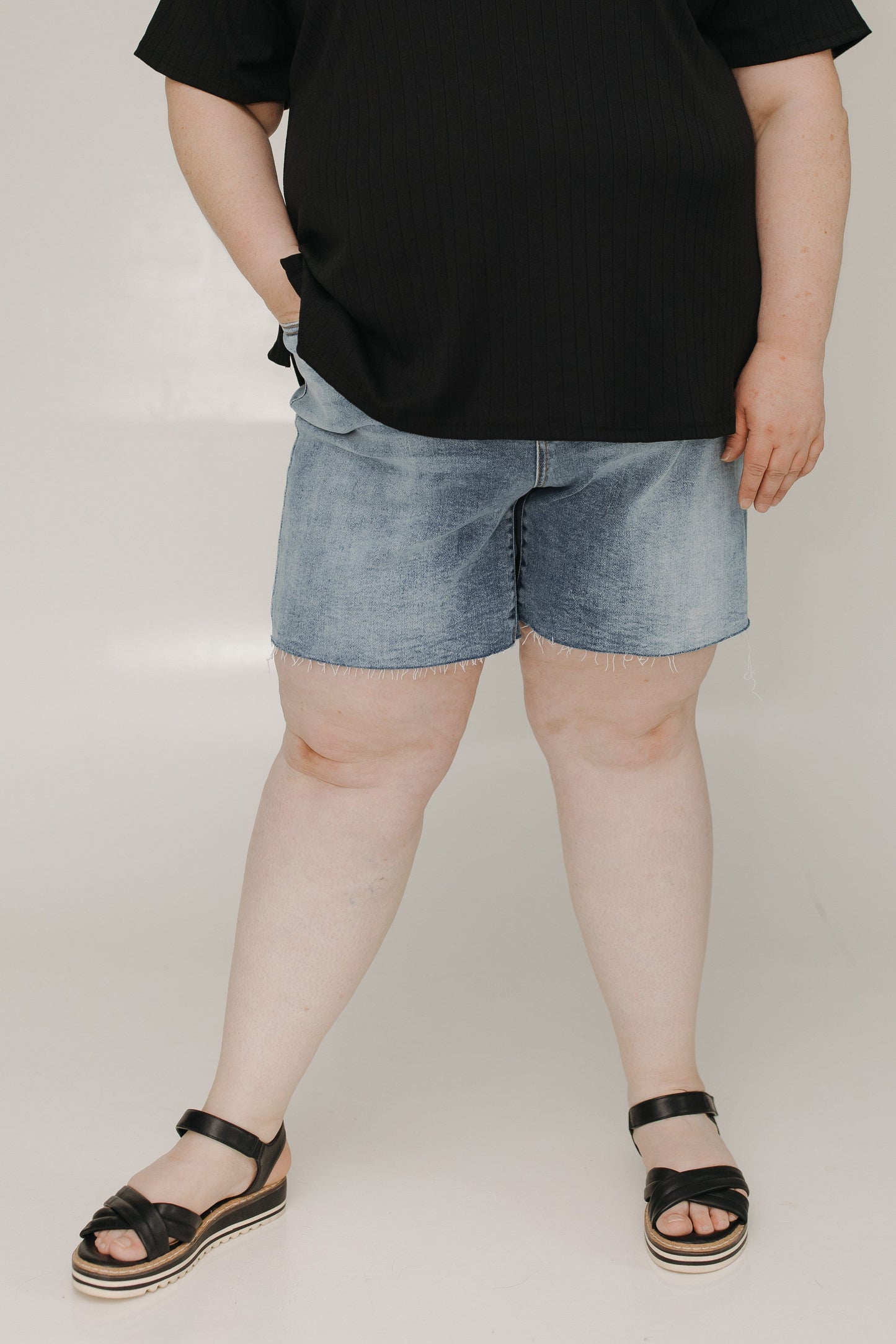 Person wearing black t-shirt and denim shorts on a plain background