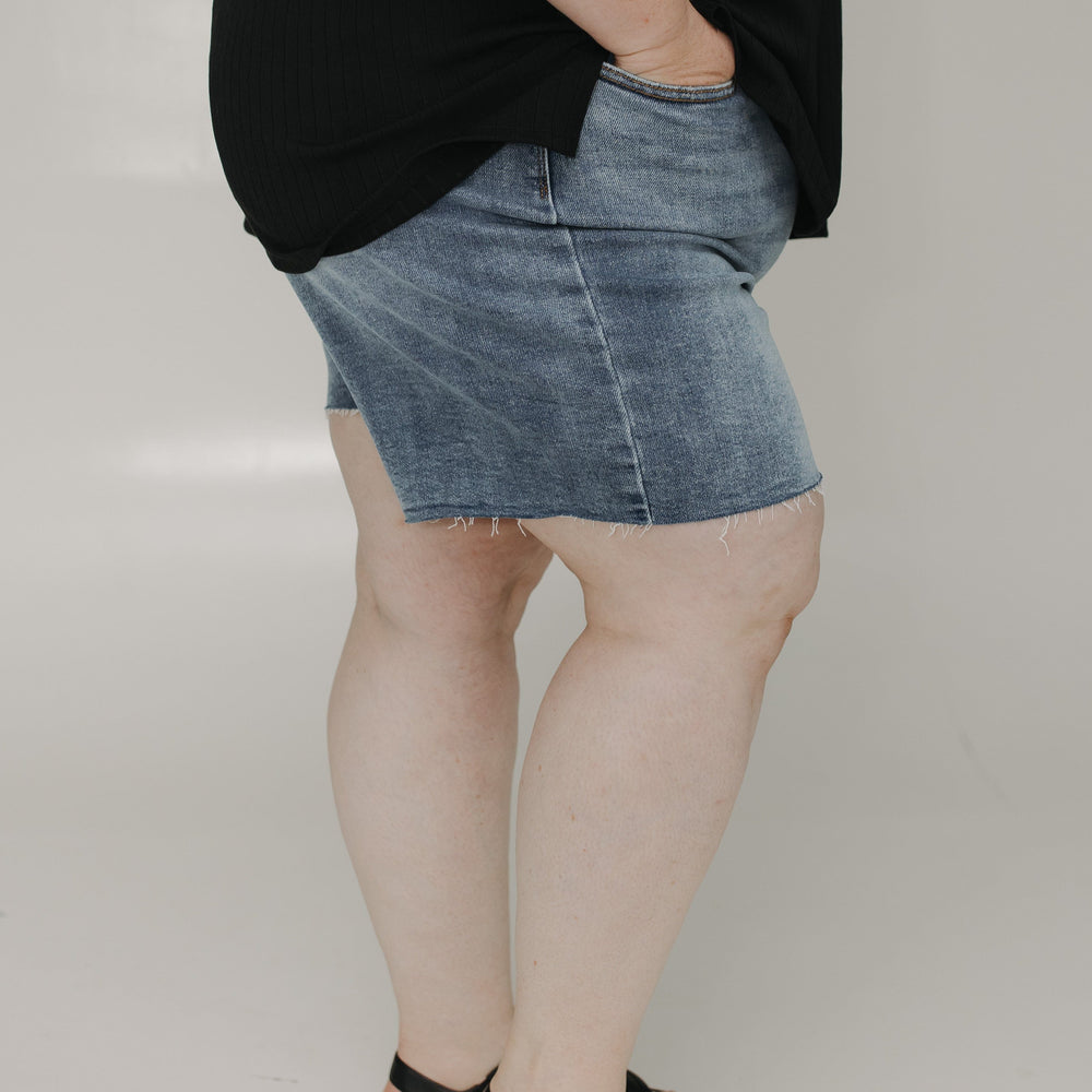 Person wearing a black top and denim skirt on a plain background