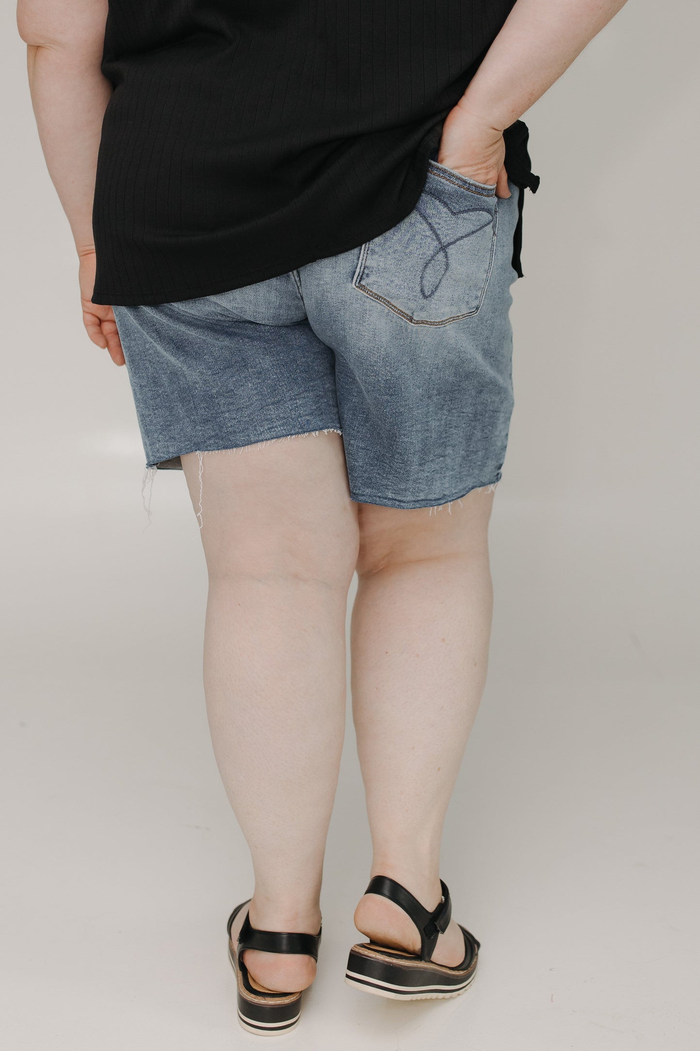Person wearing denim shorts and black sandals on a plain background