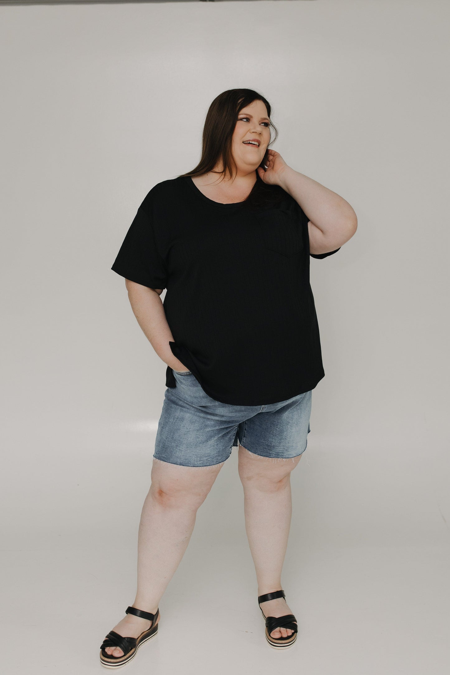 Person wearing a black t-shirt and denim shorts on a plain background