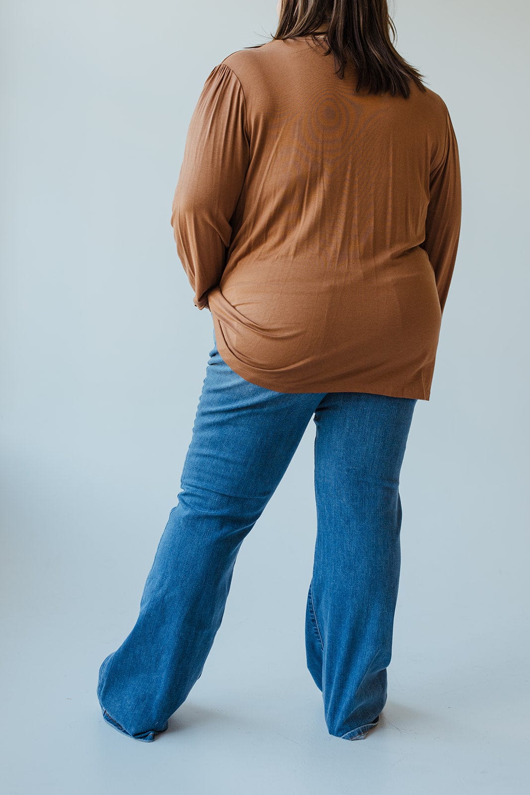 A person with long hair wearing a brown top and JUDY BLUE HIGH-WAIST NON-DISTRESSED CLASSIC FLARE IN MEDIUM BLUE by Judy Blue is facing away, standing against a plain background.