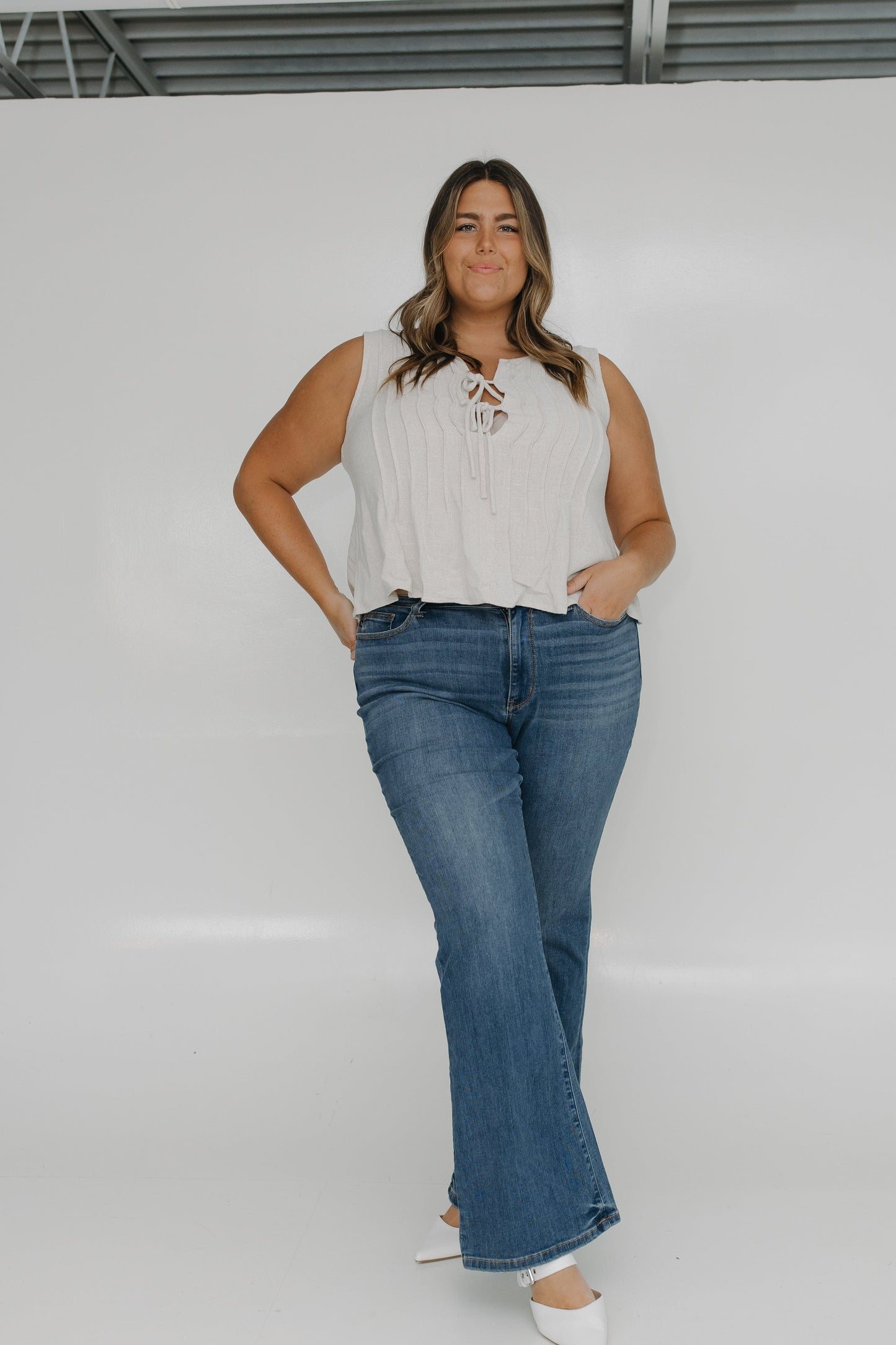 Woman wearing a sleeveless top and blue jeans against a white background